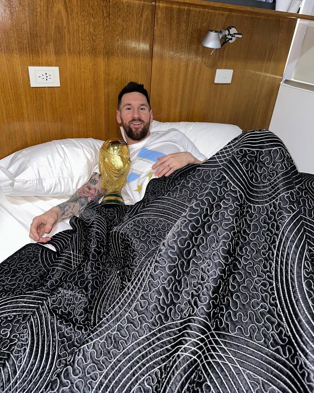 Lionel Messi posa sonriente acostado en una cama con la Copa del Mundo de la FIFA, celebrando la victoria de Argentina en el Mundial de Qatar 2022 (Instagram)