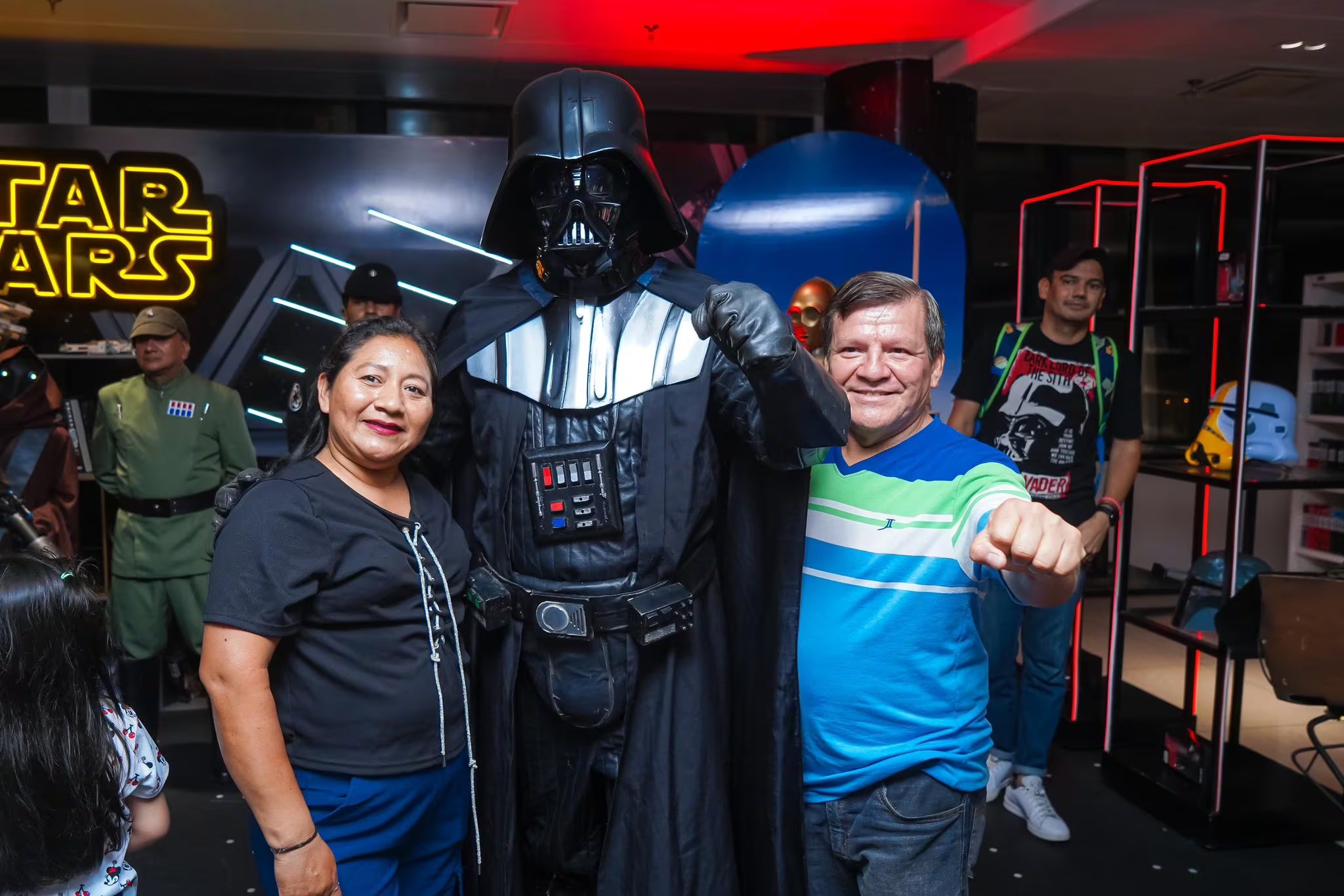 Una pareja posa con un personaje disfrazado de Darth Vader durante una exhibición temática de Star Wars en la Biblioteca Nacional de El Salvador. (Foto cortesía BINAES)