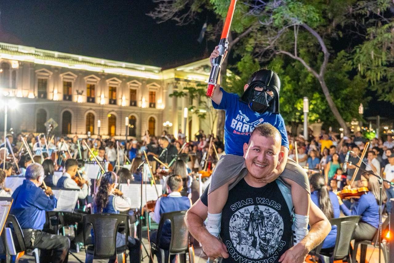 Un padre lleva a su hijo disfrazado de Darth Vader en sus hombros mientras disfrutan de la música a cargo de la Orquesta Sinfónica de San Salvador Centro. (Foto cortesía Prensa San Salvador Centro)