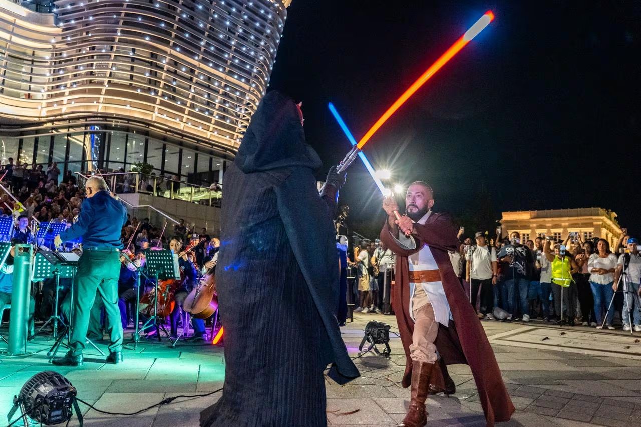 Dos artistas disfrazados de personajes icónicos de Star Wars recrean un duelo con sables de luz, acompañados por una orquesta en vivo durante un festival nocturno en pleno corazón de San Salvador. (Foto cortesía Prensa San Salvador Centro)