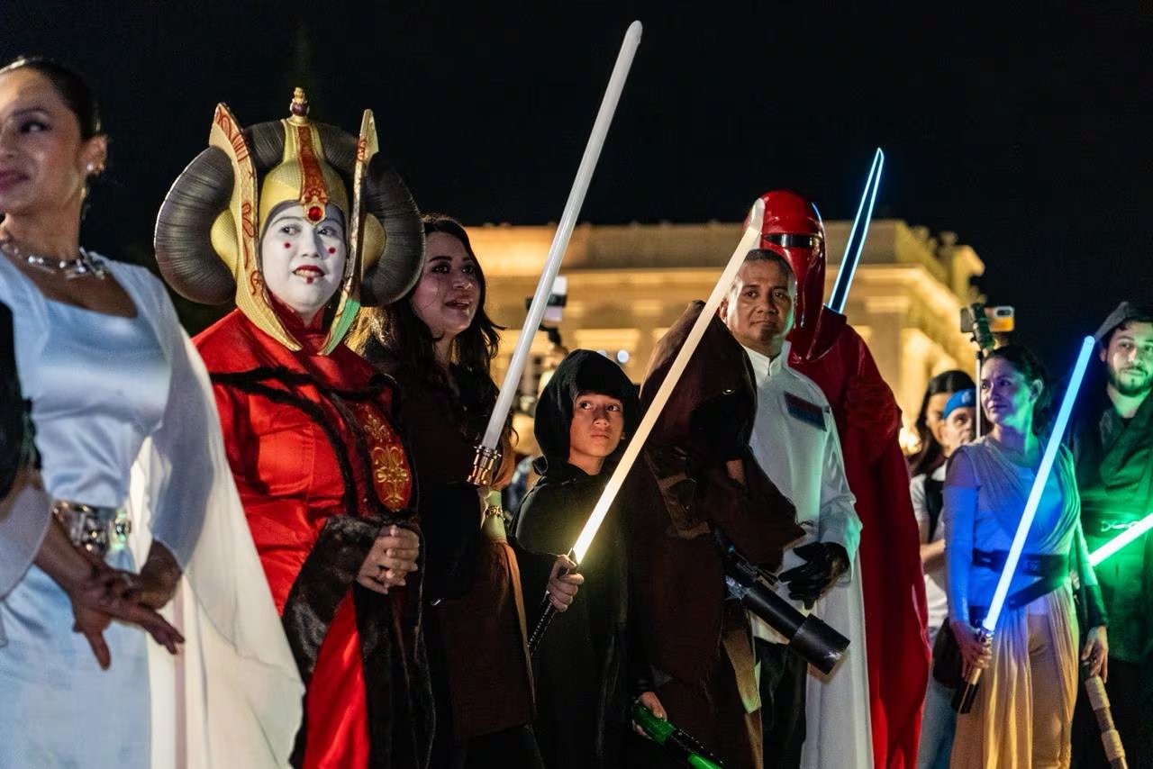 Entusiastas de Star Wars posan con sus elaborados disfraces y sables de luz encendidos durante un vibrante evento nocturno que celebra la icónica saga galáctica. (Foto cortesía)