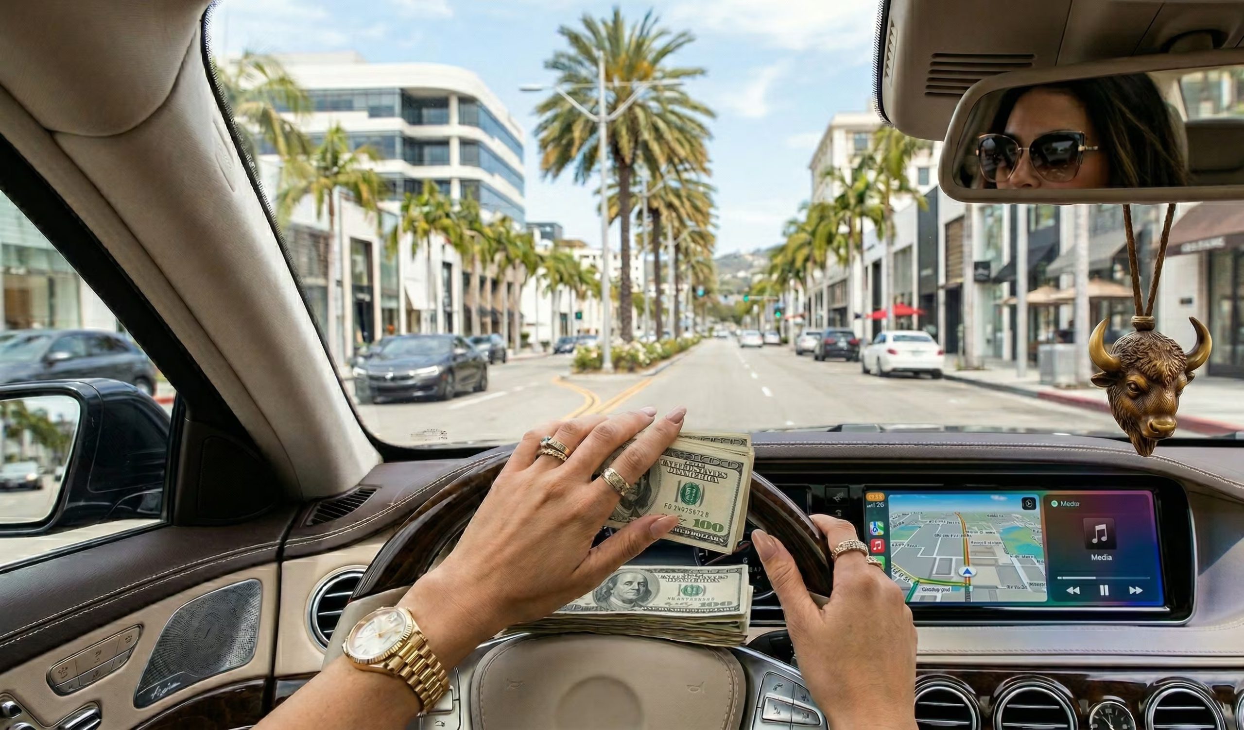 Una persona exhibe montones de billetes de cien dólares mientras conduce un coche de lujo por una avenida arbolada en California, con una mujer con gafas de sol reflejada en el espejo retrovisor. (Imagen Ilustrativa Infobae)