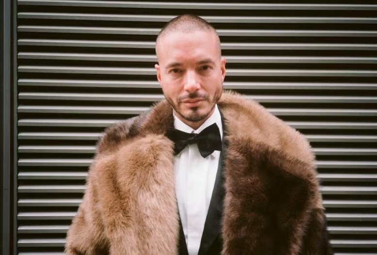 Esmoquin negro clásico con camisa blanca, pajarita negra y abrigo de piel bicolor marrón y beige en un entorno urbano de sofisticación (@jbalvin/IG)
