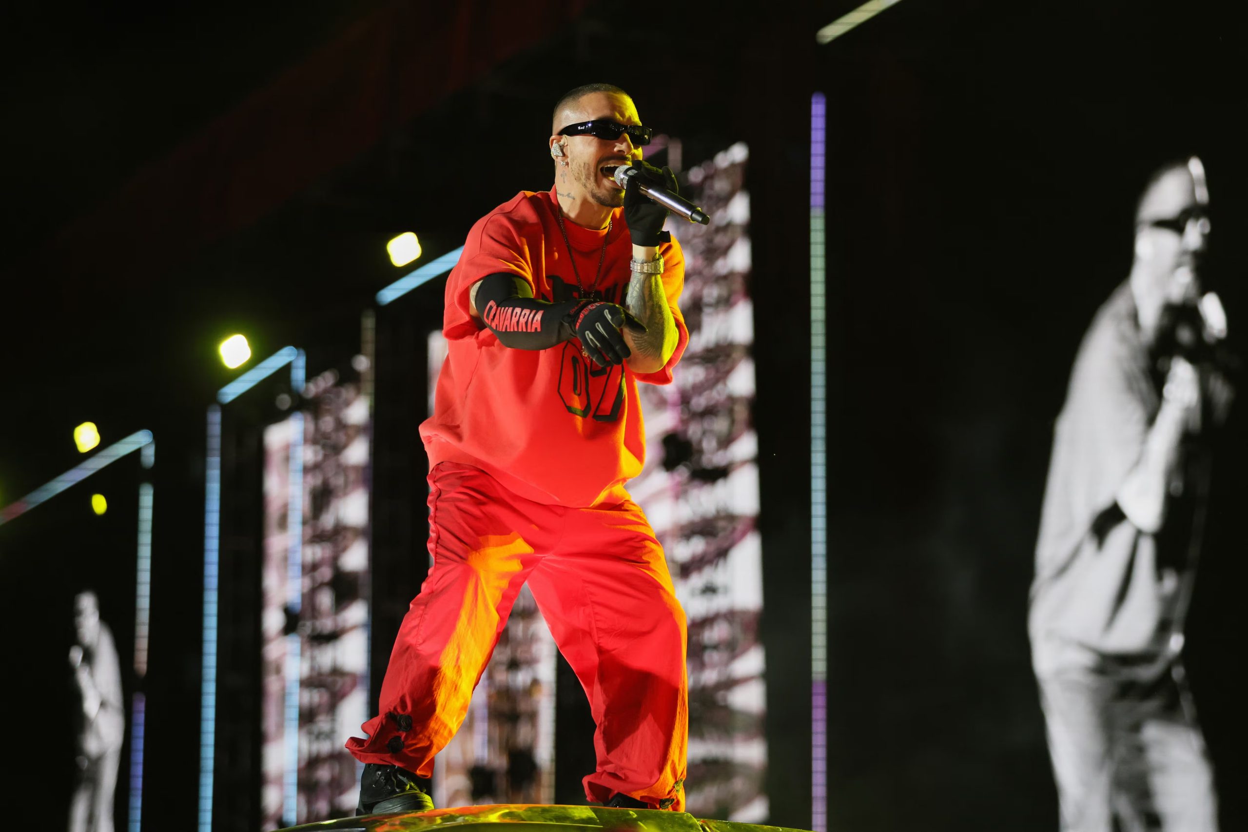Conjunto deportivo rojo con camiseta holgada número “07”, pantalón a juego, guantes negros, cadenas plateadas y gafas oscuras sobre el escenario (AP/Ginnette Riquelme)