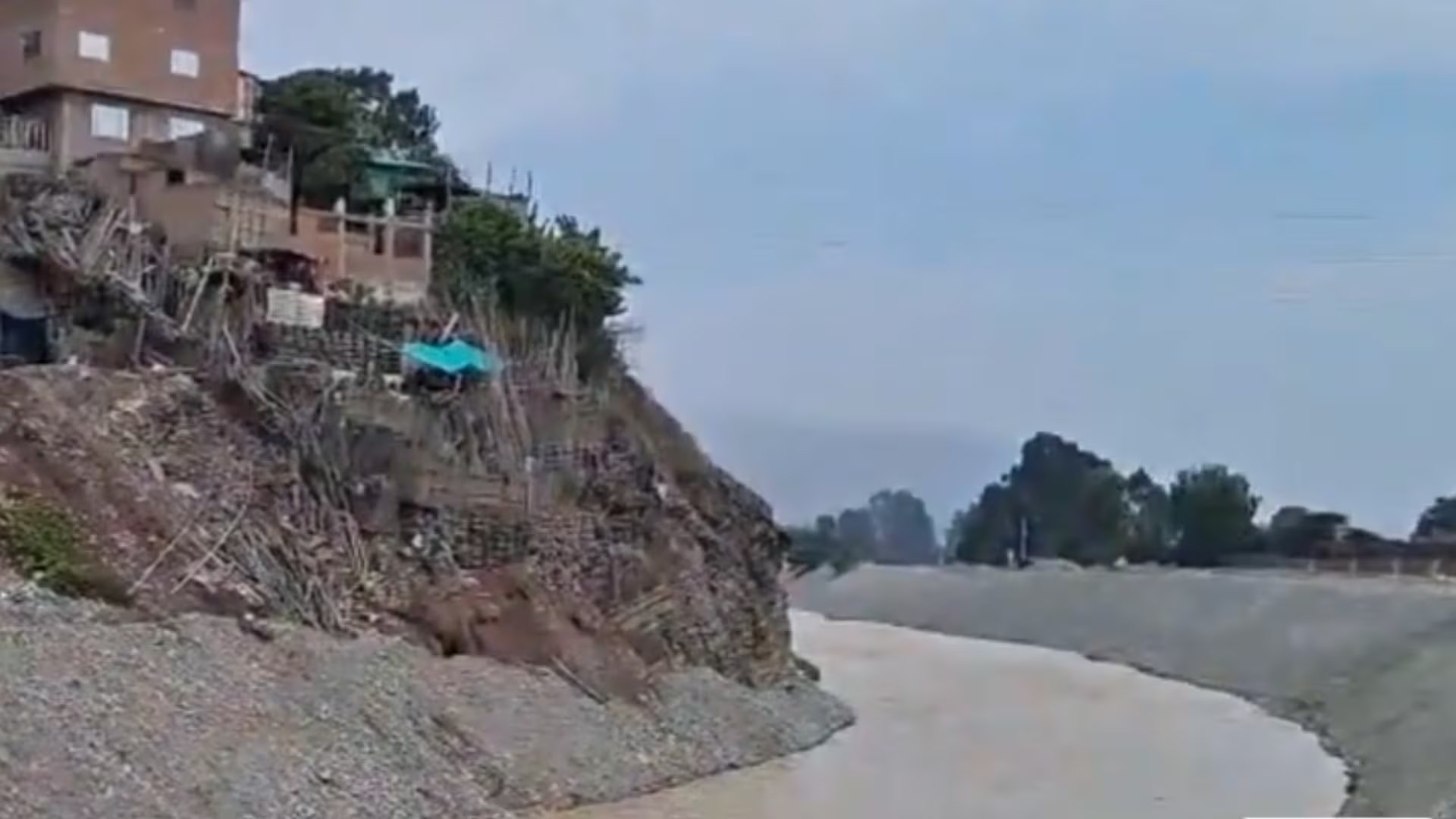 Una vivienda precaria y animales permanecen al borde del río Lurín, donde la reciente llovizna y el aumento del caudal reavivan el temor a deslizamientos y emergencias en la zona. Captura: Exitosa