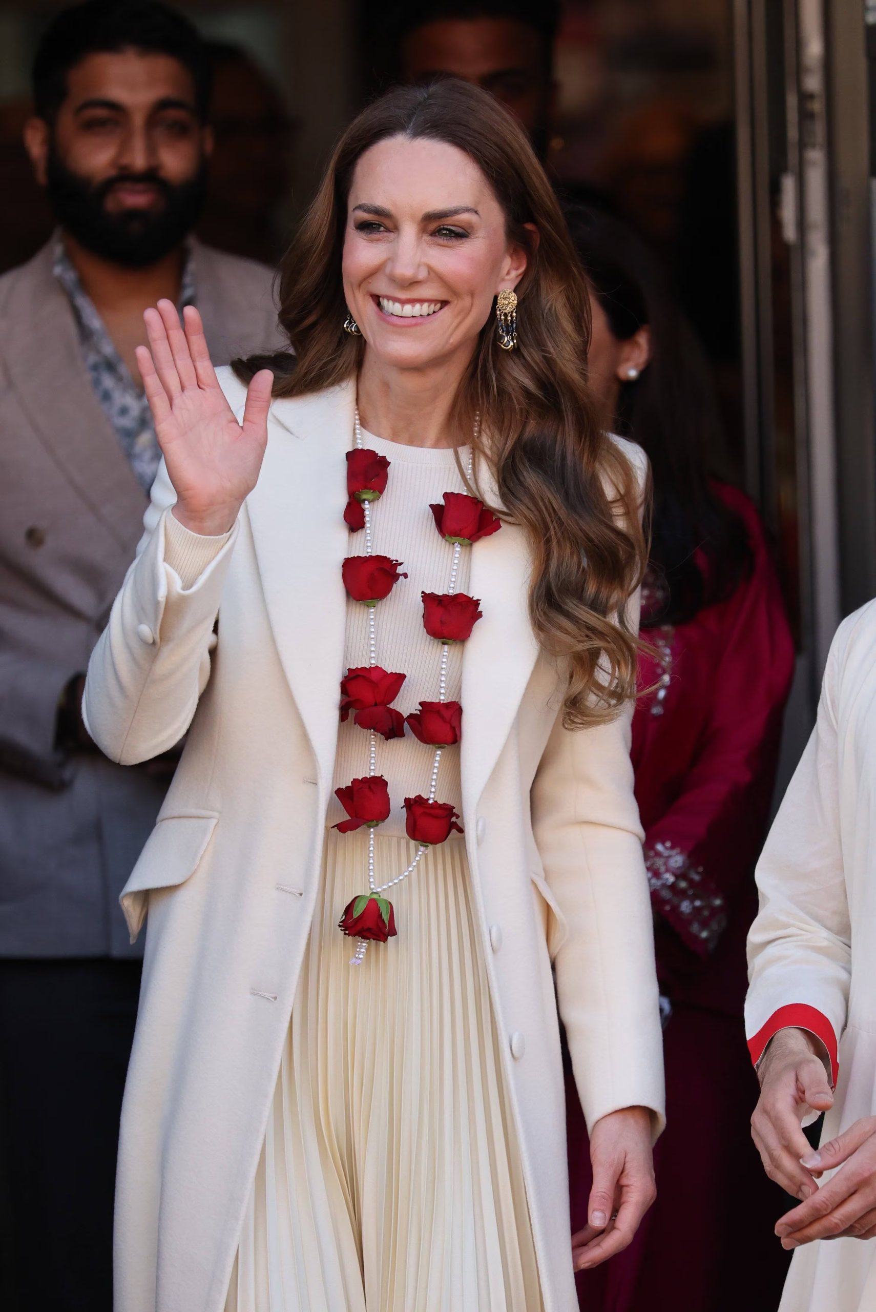 El abrigo blanco recto y el vestido plisado crema, junto al collar largo de perlas y las rosas rojas, dieron a Kate Middleton un aire institucional y refinado (Imago)