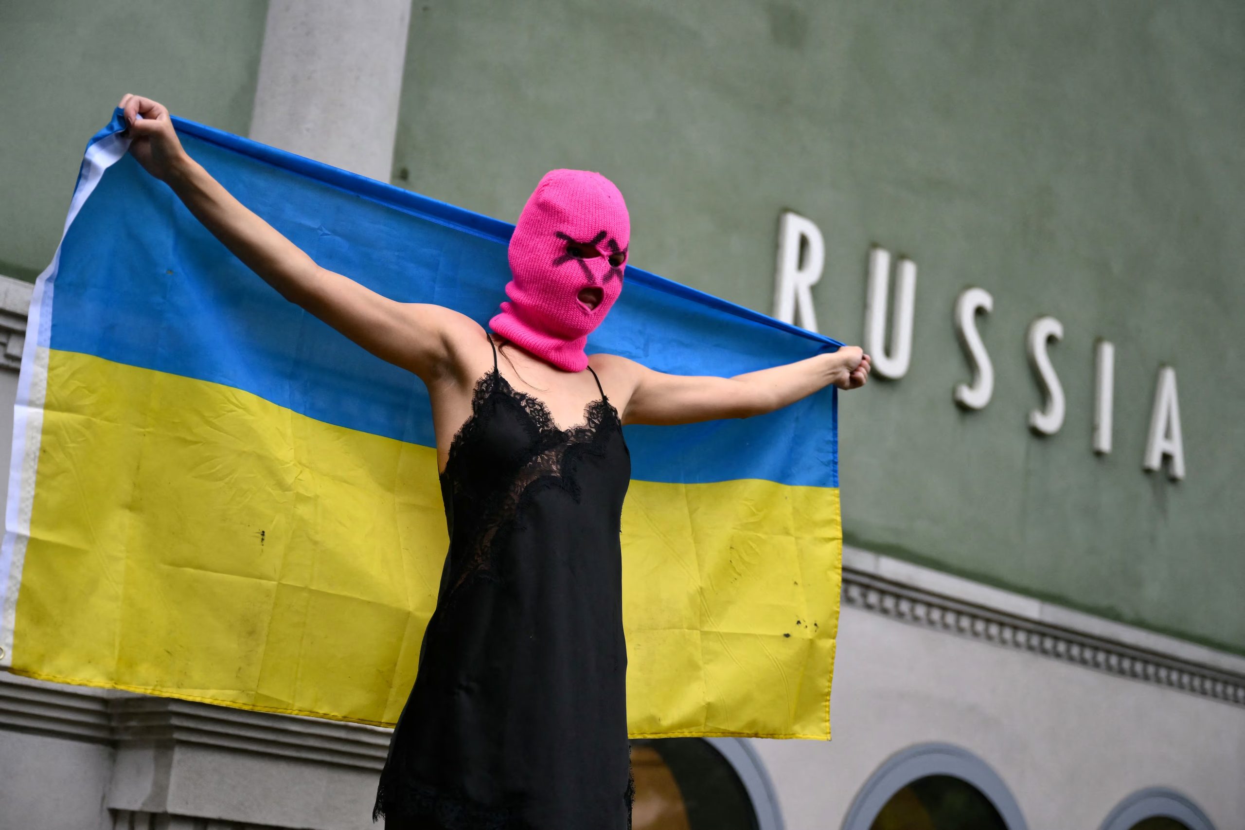 Una integrante del grupo activista Pussy Riot sostiene una bandera ucraniana durante una protesta contra la participación de Rusia (Photo by Marco BERTORELLO / AFP)