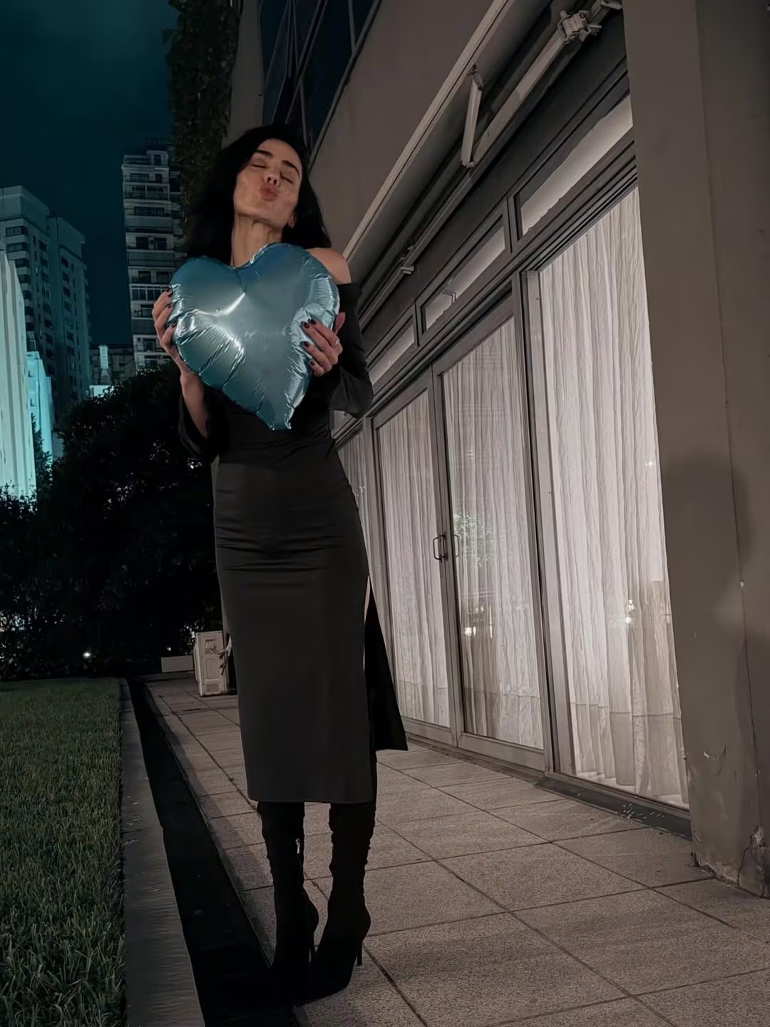 Priscila Crivocapich, celebrando su cumpleaños, posa con un globo de corazón azul en un elegante entorno urbano nocturno.