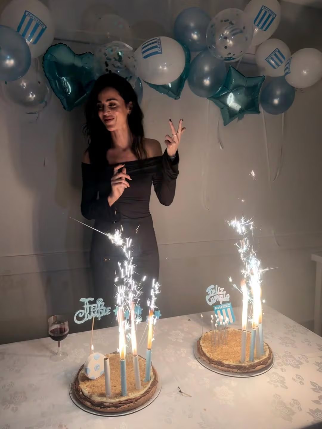 Priscila Crivocapich sonríe mientras celebra su cumpleaños rodeada de globos de Racing Club y dos tortas con bengalas en un ambiente festivo.