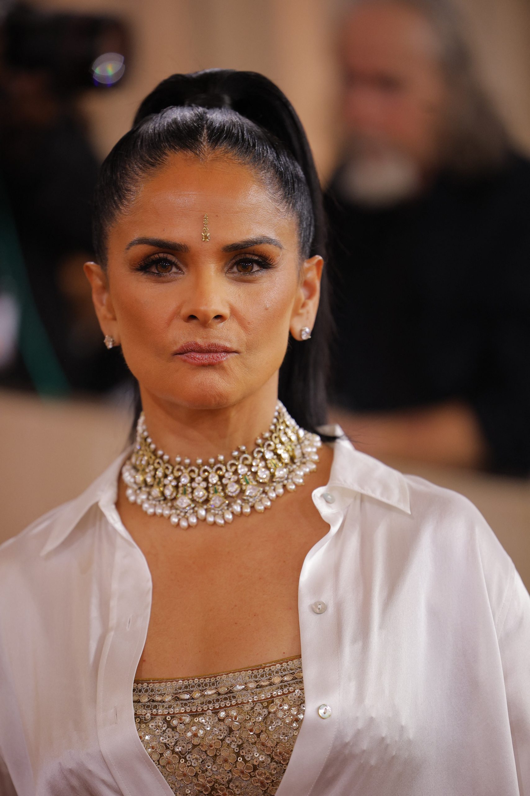 La camisa blanca satinada de Bela Bajaria, acompañada de un top dorado con lentejuelas, suma luminosidad y sofisticación a la combinación de texturas y brillos que marcan su estilo (REUTERS/Mike Blake)