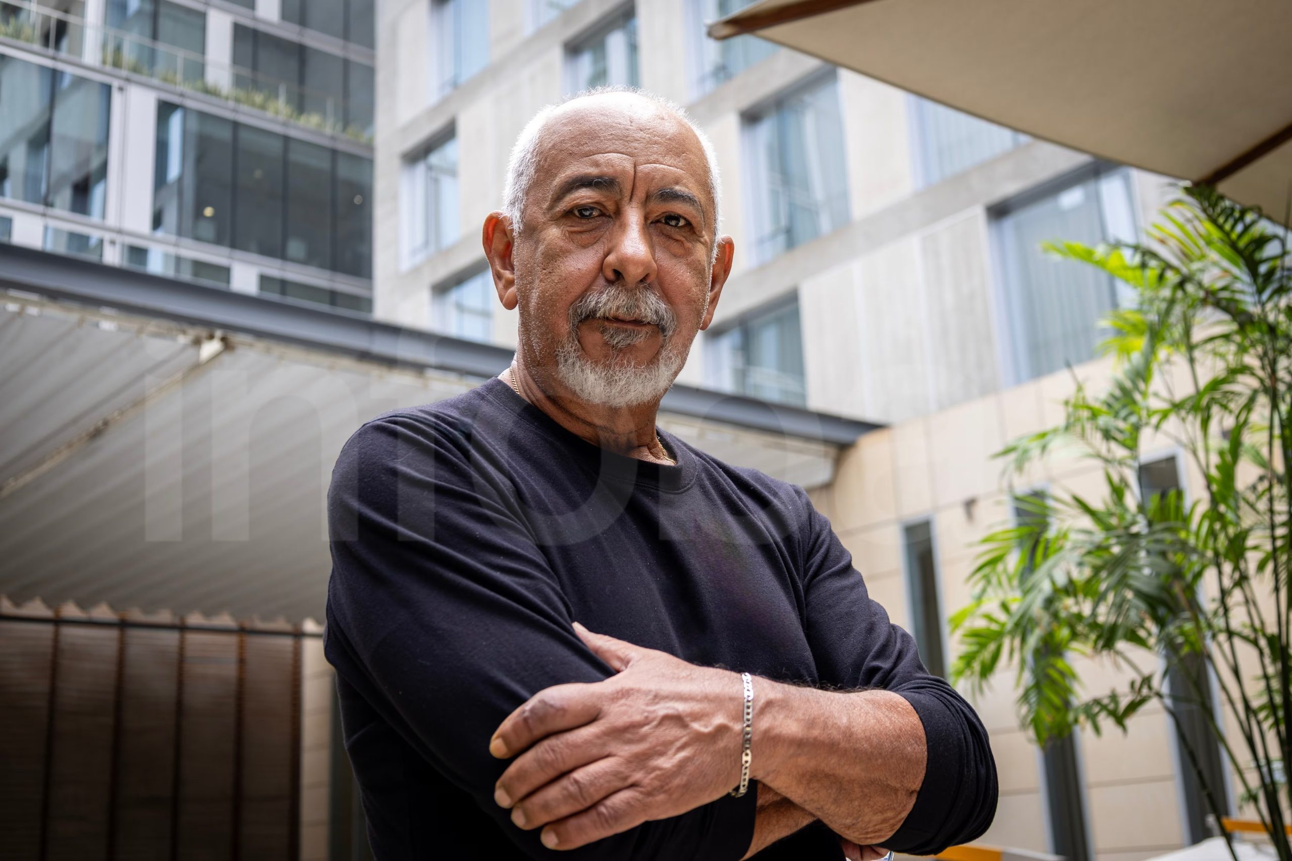 El escritor cubano Leonardo Padura posa con los brazos cruzados ante un fondo de edificios modernos y vegetación. (Paula Elizalde)