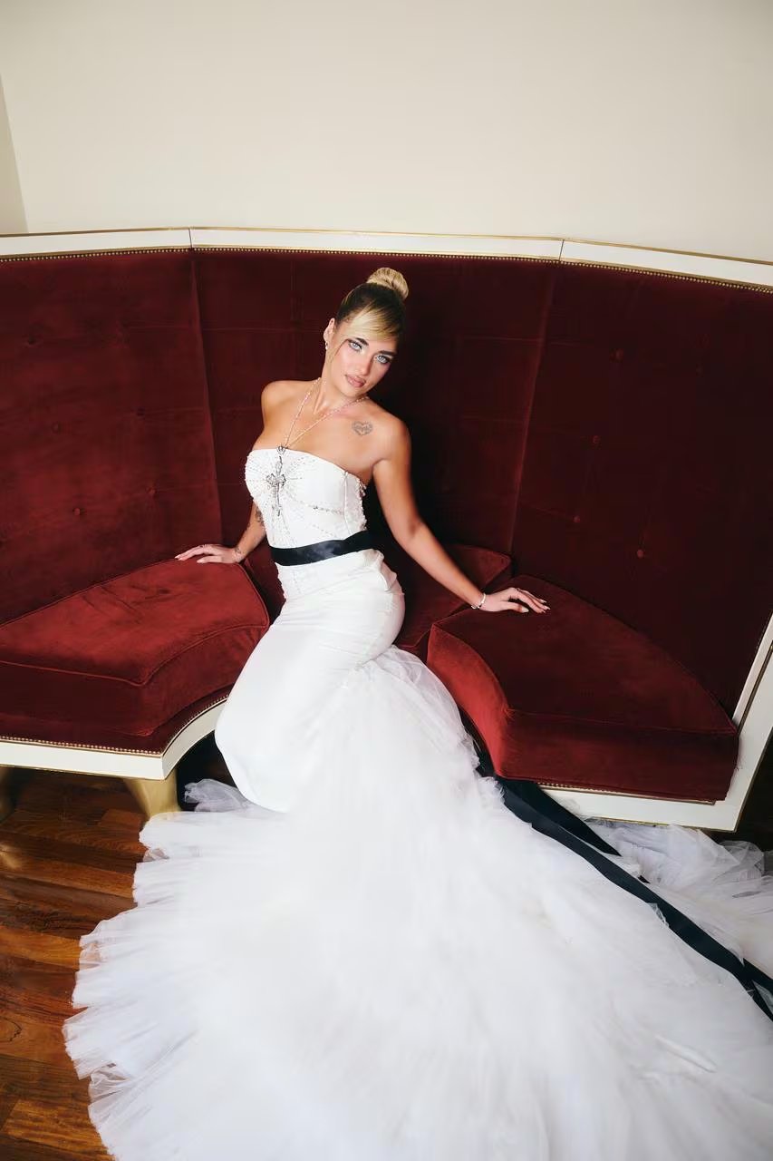 Marta Fort luce un impactante vestido blanco con falda de tul y un lazo negro, sentada en un sofá rojo, para los premios Martín Fierro de la Moda.