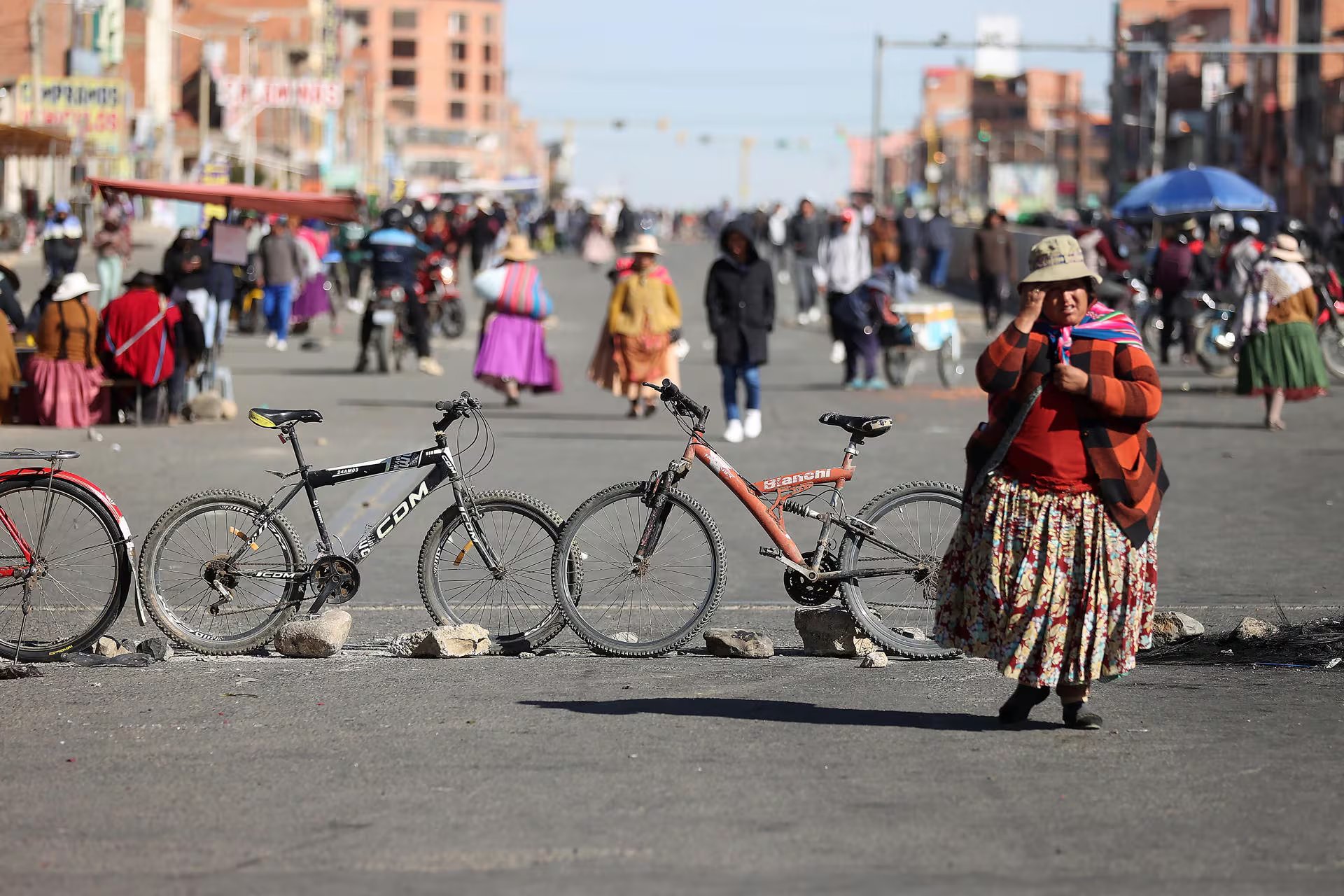 Una mujer camina junto a dos bicicletas y rocas que bloquean una calle concurrida en La Paz, donde el tráfico de personas continúa a pesar de la interrupción
