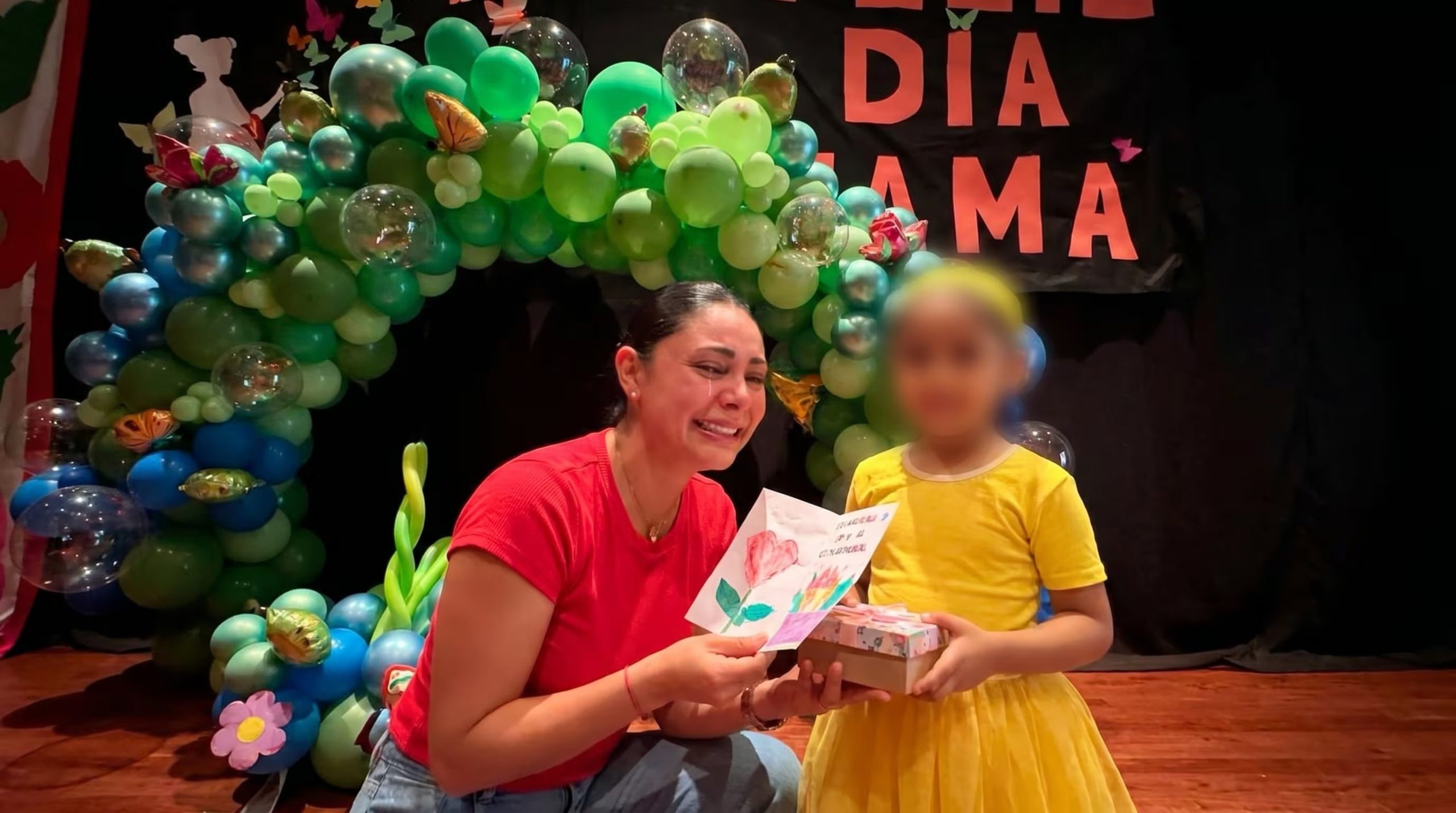 Pamela Franco visiblemente conmovida mientras su hija María Cataleya le entrega un dibujo y un regalo por el Día de la Madre, con una decoración de globos de fondo. (Imagen Ilustrativa Infobae)
