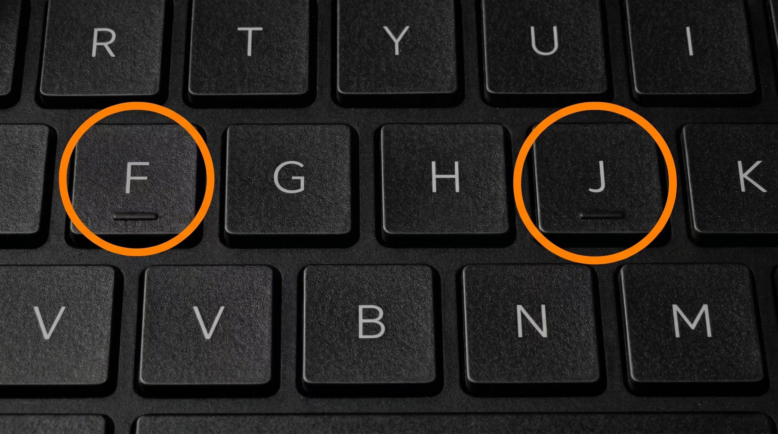 Vista de cerca de un teclado de laptop negro donde las teclas F y J están claramente resaltadas con círculos naranja, indicando su importancia para la digitación táctil. (Imagen Ilustrativa Infobae)