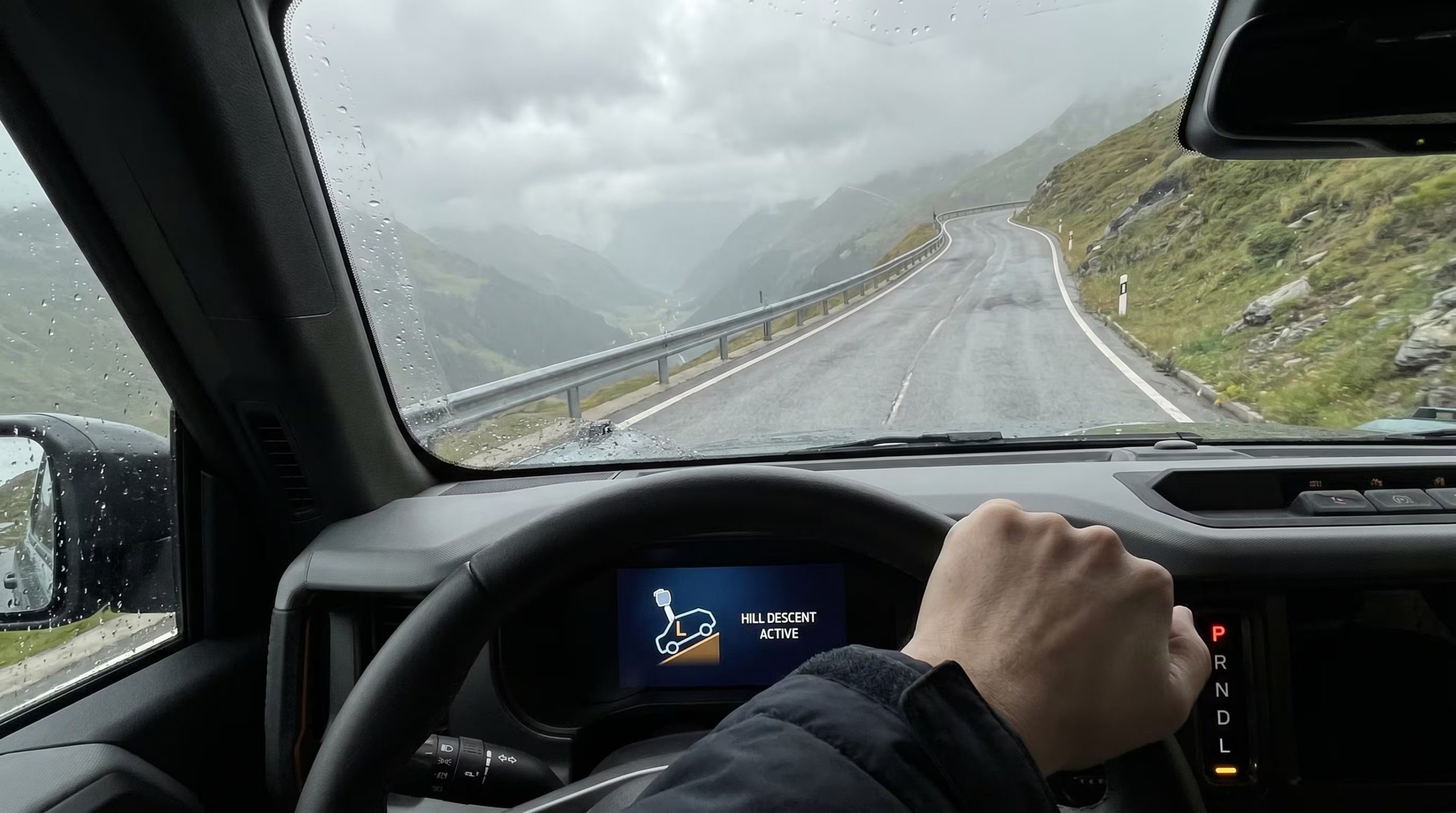 Un conductor utiliza el modo 'L' de la transmisión en un vehículo automático para descender una empinada carretera de montaña bajo un cielo nublado, evidenciando una conducción segura y tecnológica. (Imagen Ilustrativa Infobae)