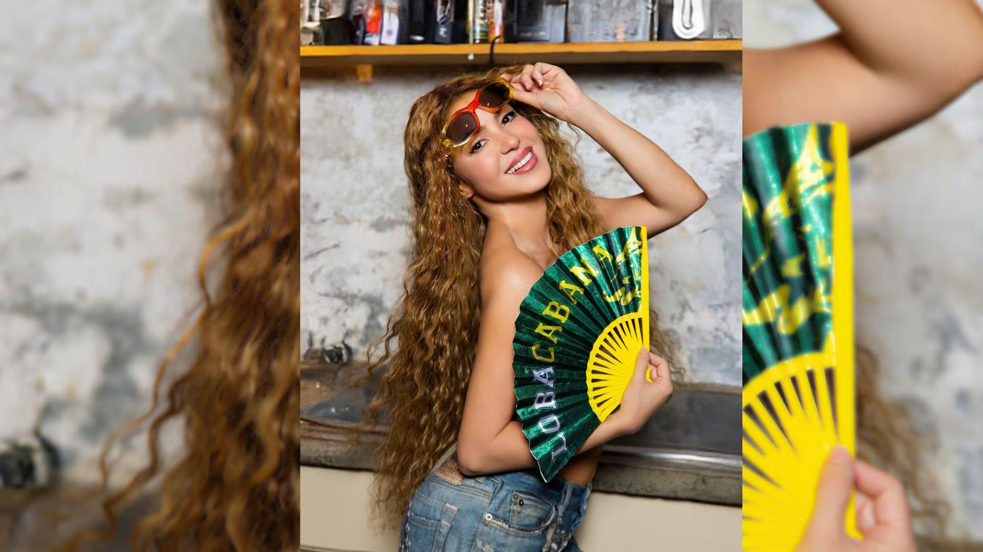 La artista Shakira sonríe a la cámara, luciendo un atuendo casual con jeans y sosteniendo un abanico verde y amarillo con el texto 'Loba Cabana' en una sesión para YouTube Music. (Instagram: shakira)