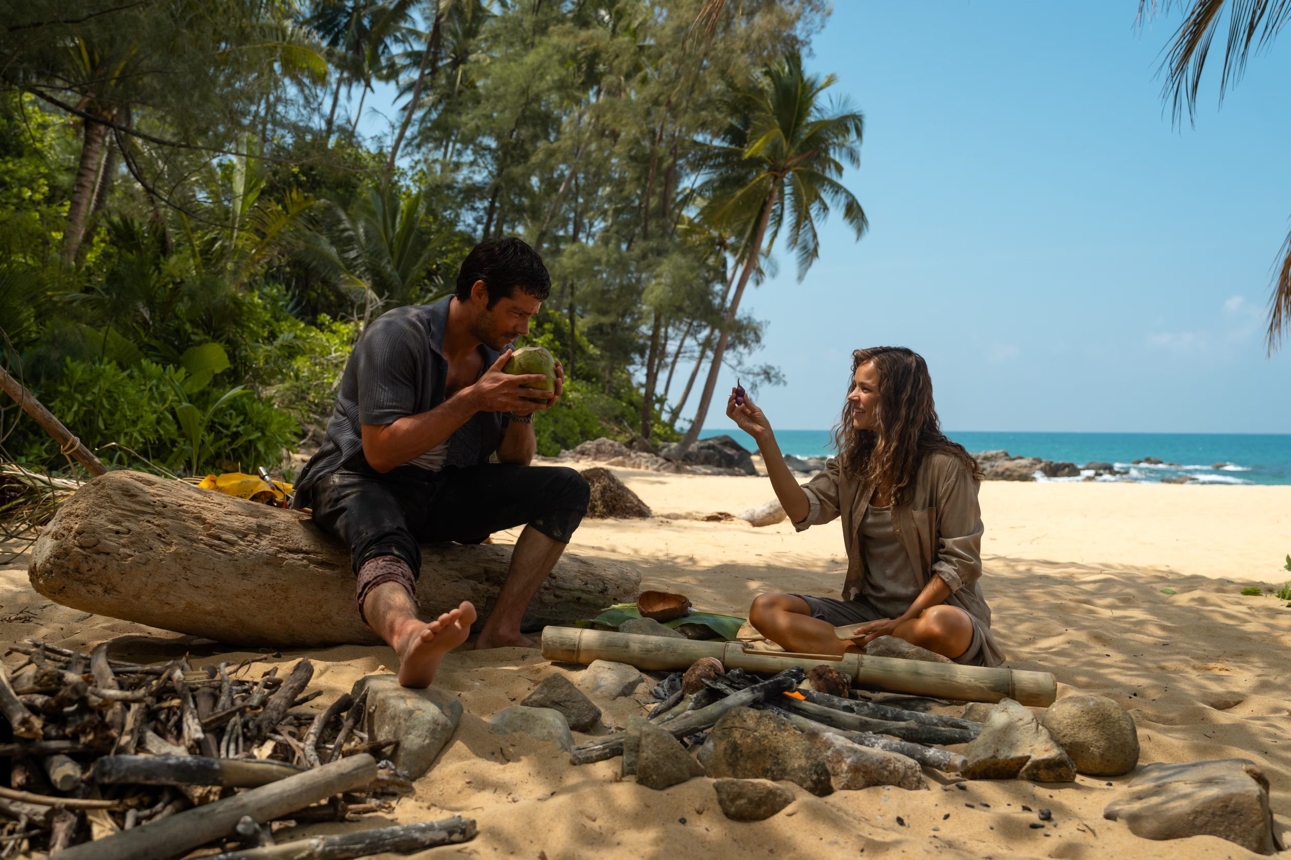 Rachel McAdams y Dylan O'Brien se refugian en una playa tropical, compartiendo lo que recolectaron para sobrevivir junto a una fogata improvisada (Disney)