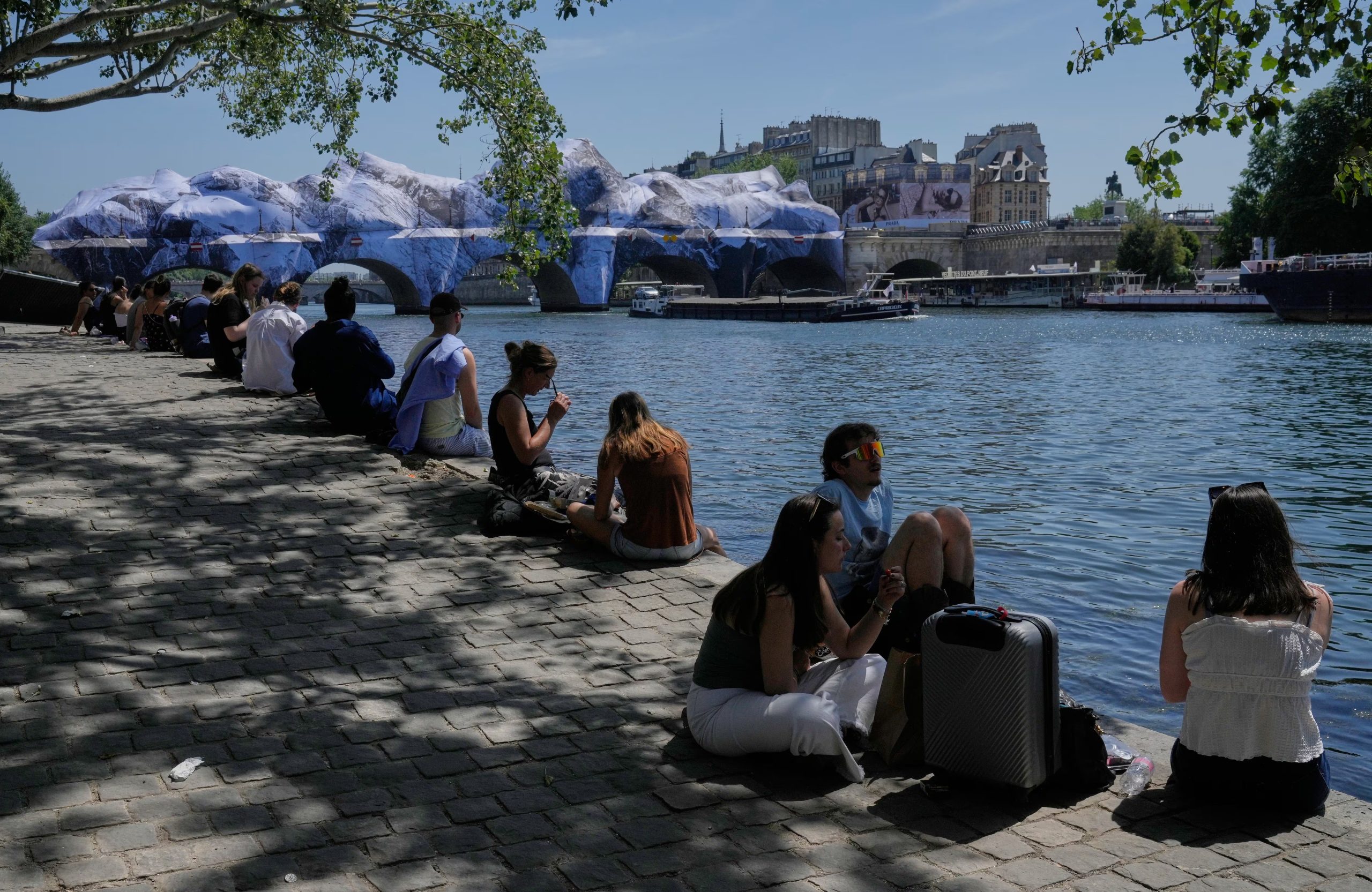 Parisinos buscan alivio del calor a orillas del Sena, con una obra del artista callejero JR sobre el Puente Nuevo de fondo, un día antes de que Francia registrara su temperatura más alta en un mes de mayo desde que hay registros. (AP Photo/Michel Euler)