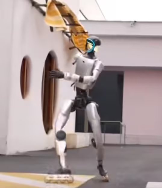 Un robot humanoide plateado con un visor azul sostiene una tabla de surf a rayas mientras se encuentra en una posición dinámica frente a un edificio blanco con ventanas ovaladas.