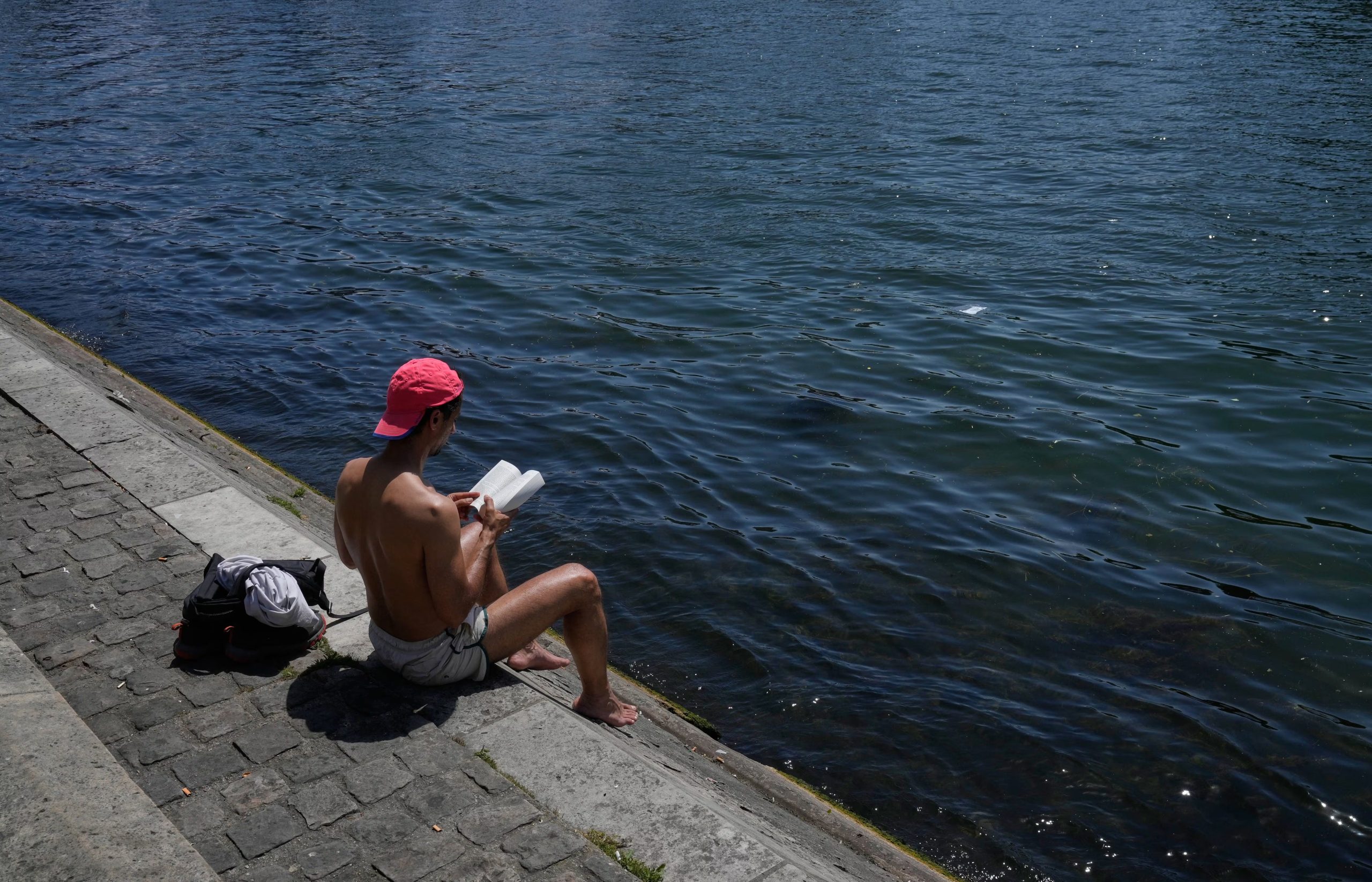 Un hombre lee un libro sentado al sol a orillas del río Sena, en París. (AP Foto/Michel Euler)