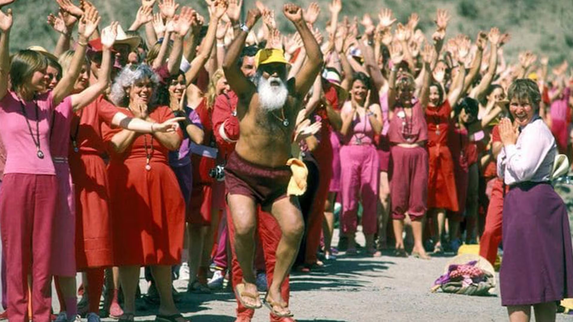 Osho saltando frente a una multitud de seguidores vestidos de rojo, un momento capturado en el documental Wild Wild Country