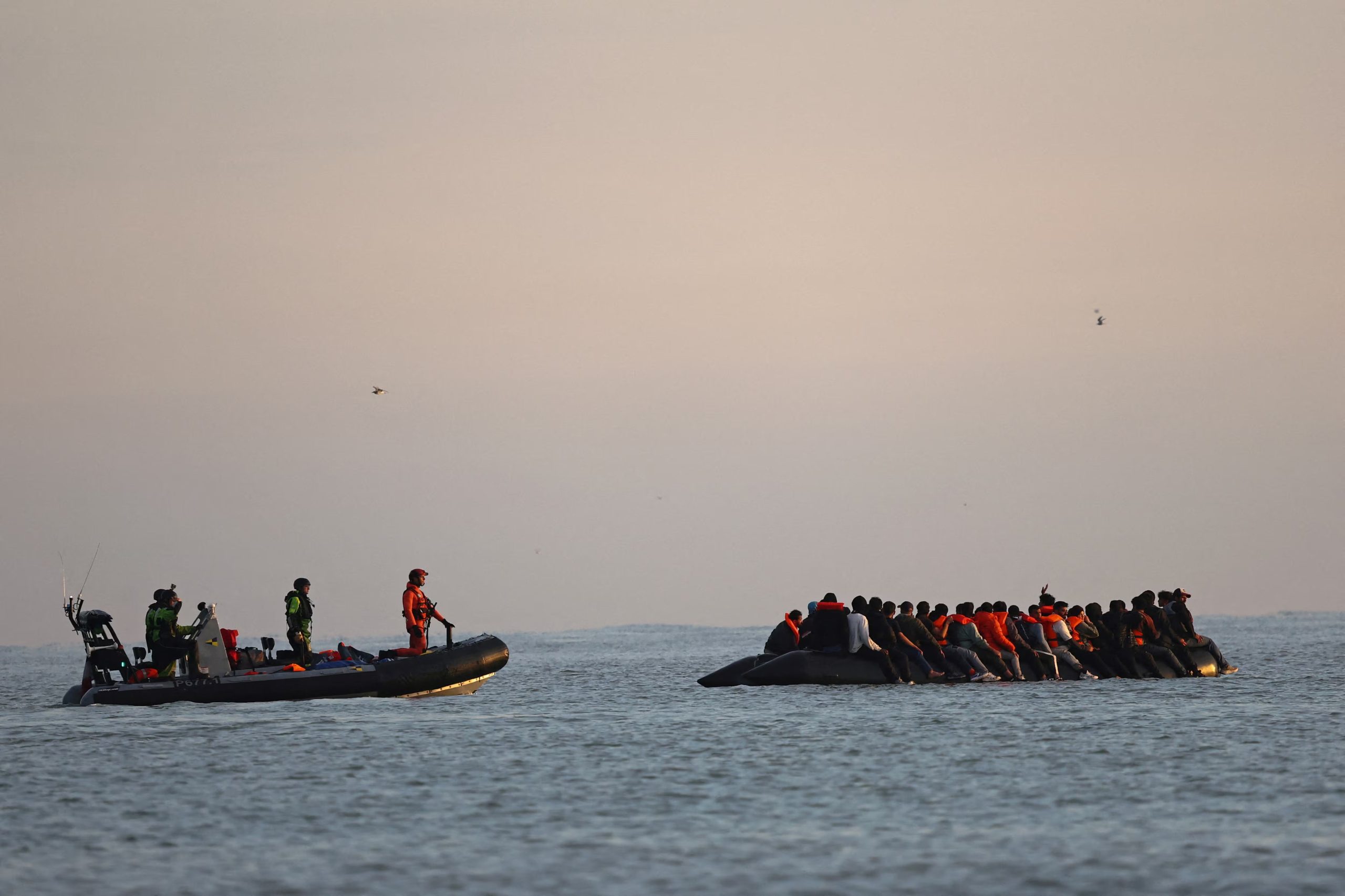 Gendarmes franceses se acercan a un grupo de migrantes a bordo de un bote inflable que intenta cruzar el Canal de la Mancha hacia Gran Bretaña, desde la playa de Petit-Fort-Philippe, cerca de Calais, Francia, en julio de 2025 (REUTERS/Gonzalo Fuentes, archivo)