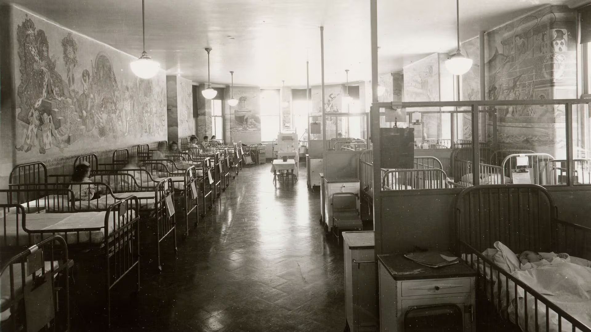 La sala de pediatría del Hospital Gouverneur después de una renovación en 1939-40, con pequeños pacientes en sus camas contemplando el mural de Alicia de Champanier que envuelve las paredes (Archivos Municipales, Ciudad de Nueva York)