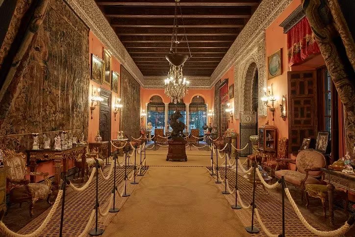 El impresionante salón principal del Palacio de las Dueñas en Sevilla, adornado con tapices, mobiliario antiguo y elementos decorativos.