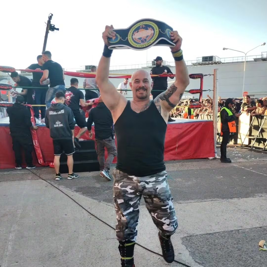 El luchador Pablo Más Albert, conocido como Teniente Murphy de 100% Lucha, sostiene el cinturón de campeón durante su despedida en un evento al aire libre.