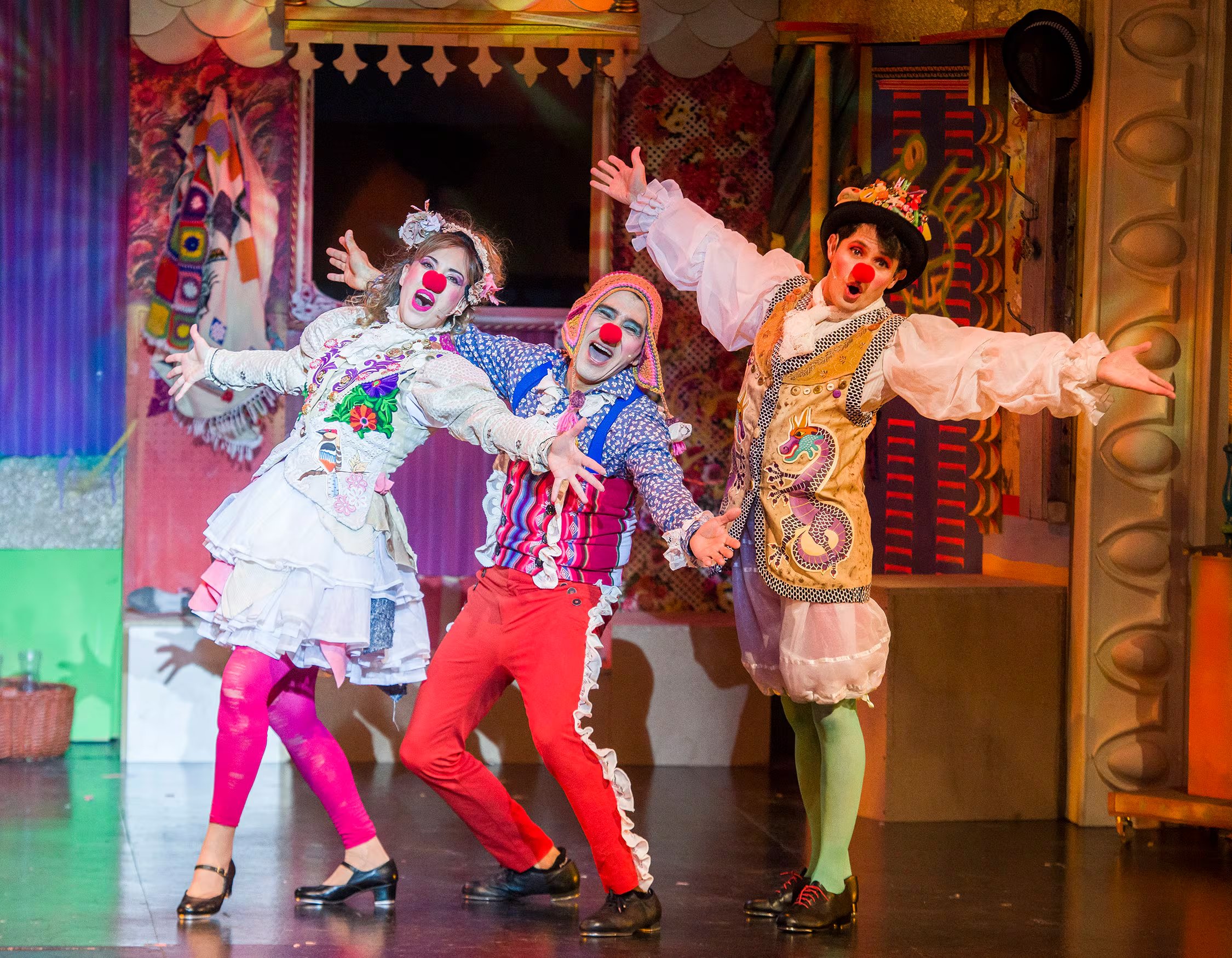 Una escena de la obra teatral Vivitos y coleando 2 muestra a los actores Osqui Guzmán, Flavia Pereda y Julián Pucheta con vestuarios de colores vivos y narices rojas.