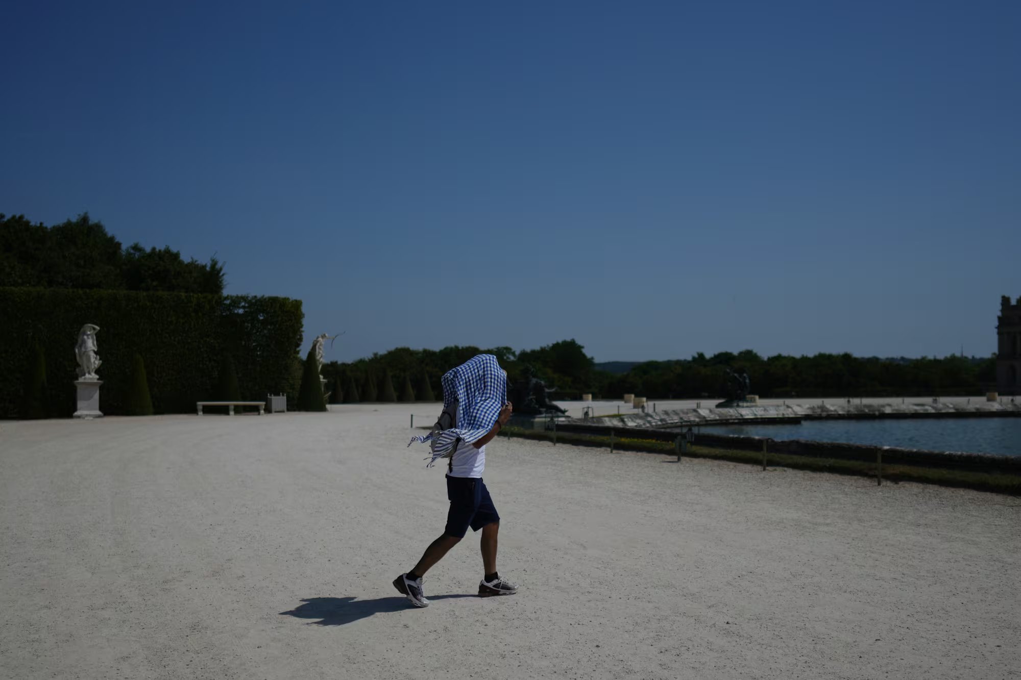 Un hombre se cubre del sol con un pañuelo en los jardines de Versalles, cerca de París, el 22 de junio de 2026, en medio de la ola de calor que afecta a Francia. (Foto AP/Thibault Camus)