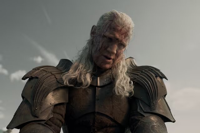 El príncipe Daemon Targaryen, con cicatrices de batalla y armadura oscura, aparece en una escena de la serie
