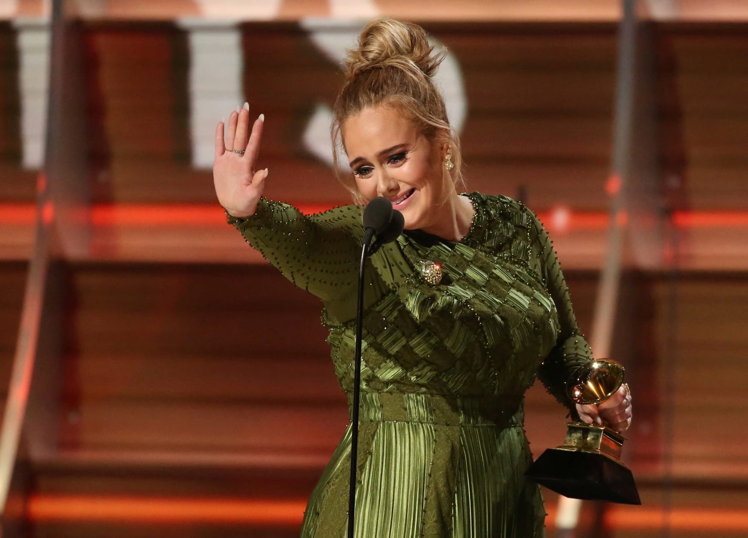 Sobre el escenario, Adele viste un diseño verde oliva plisado con pedrería en corsé y mangas, rematado con recogido alto y pendientes dorados (REUTERS/Lucy Nicholson/File Photo)