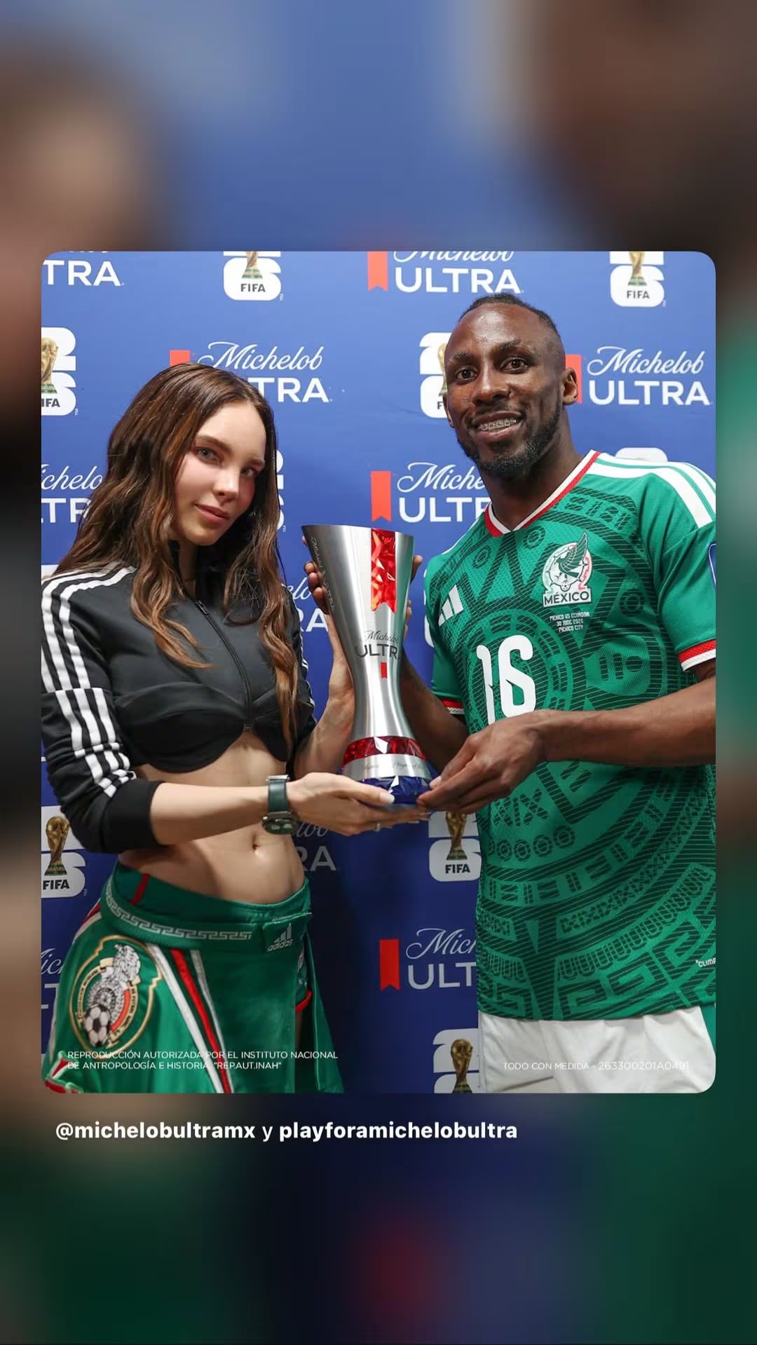 Belinda y Julián Quiñones posan con el trofeo de Jugador Más Valioso frente a un fondo azul con logotipos de Michelob Ultra y FIFA. (Instagram: Belinda)