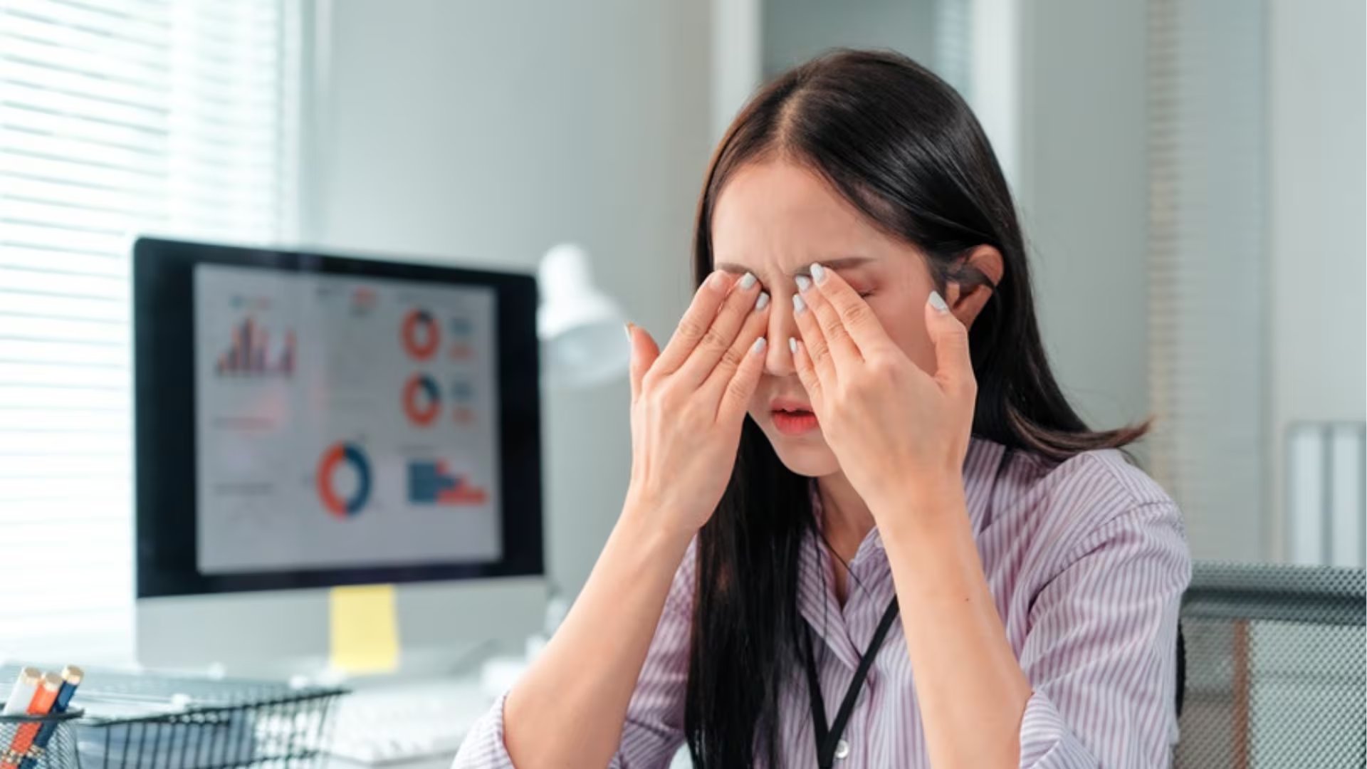 Una mujer se frota los ojos en su puesto de trabajo, ilustrando el malestar visual asociado al Síndrome del Ojo de Invierno que incide en la productividad laboral en Lima.