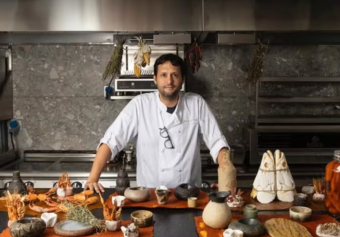 El chef peruano Jaime Pesaque posa en una cocina profesional rodeado de ingredientes frescos y piezas de cerámica para su nuevo restaurante en Nueva York.