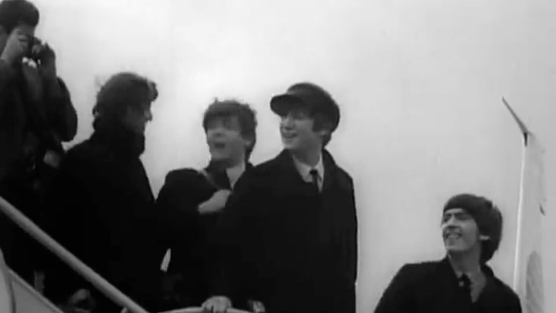 Los miembros de The Beatles, John Lennon, Paul McCartney y George Harrison, sonríen mientras descienden, capturando la esencia de su fama mundial y la efervescencia de la Beatlemania durante una convención (Captura de video)