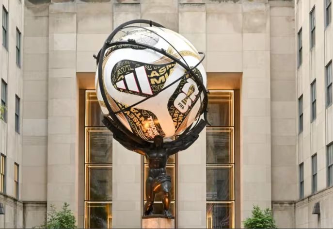 Una estatua exhibe una réplica del balón Adidas Trionda Final del Mundial 2026 en un contexto urbano, con edificios de fondo.