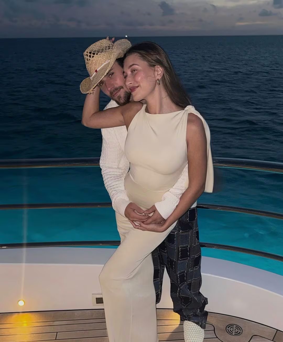 Hailey Bieber destaca con un mono beige asimétrico de pantalón acampanado, y Justin Bieber acompaña con suéter blanco de punto, pantalón oscuro a cuadros y sombrero de paja (Créditos: Instagram/Hailey Williams)