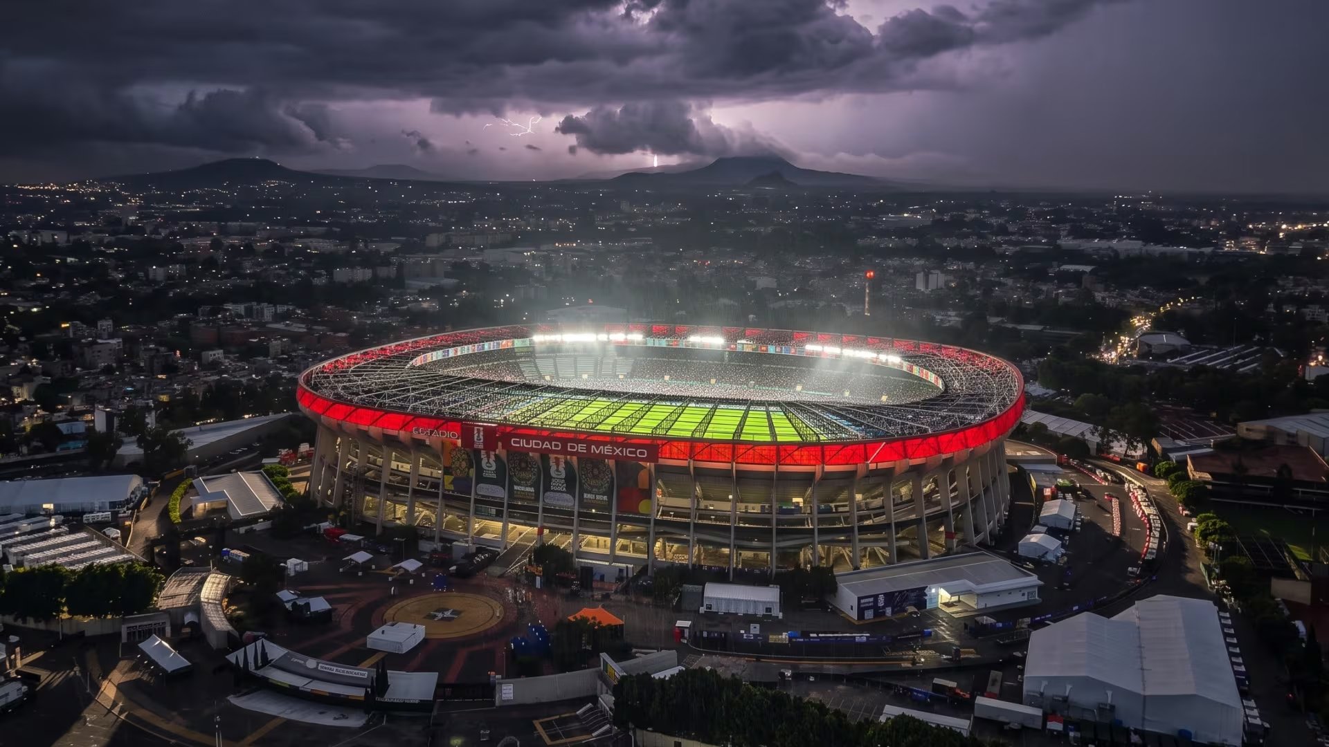 El Estadio Ciudad de México se ilumina bajo un cielo con tormenta eléctrica, mostrando su campo verde y la ciudad en la noche. (Imagen ilustrativa IA Infobae)