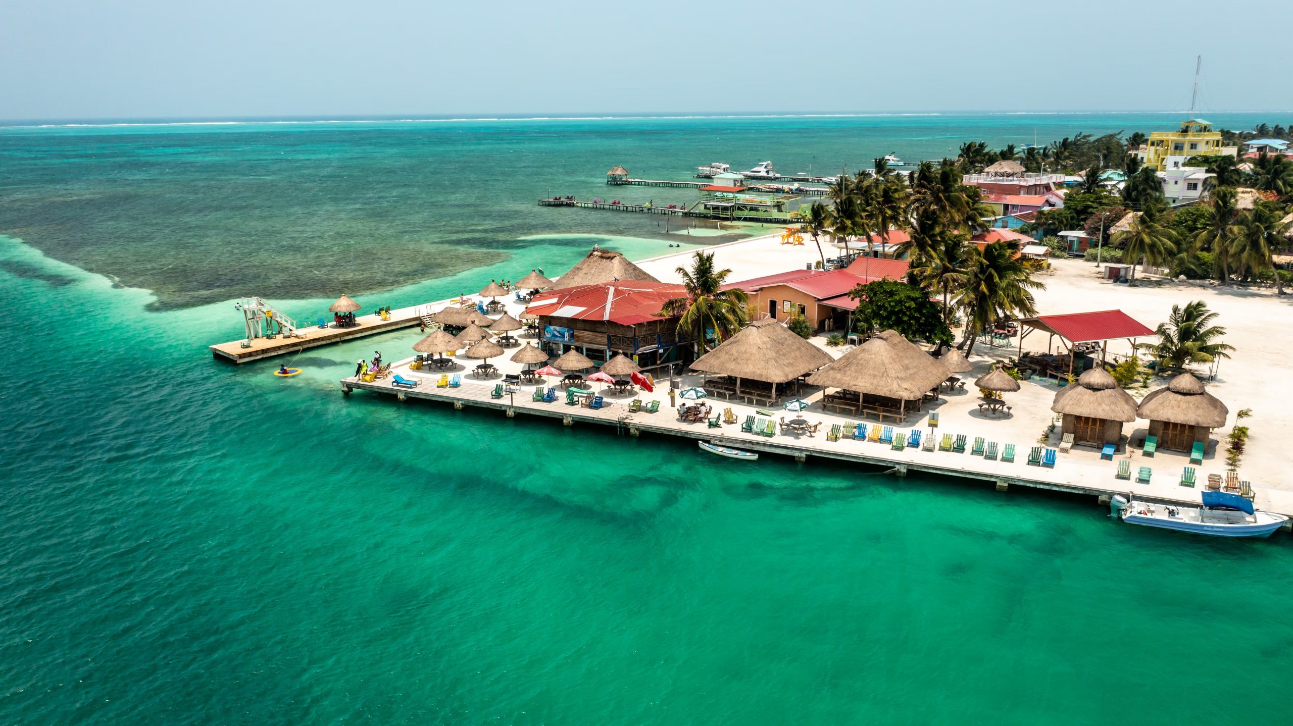 Una panorámica aérea muestra el Sea Crest Oceanfront Resort con sus estructuras de techo de paja, muelles, embarcaciones y aguas cristalinas en Caye Caulker. (The Belize Tourism Board (BTB), órgano del Ministerio de Turismo y Relaciones con la Diáspora de Belice.)