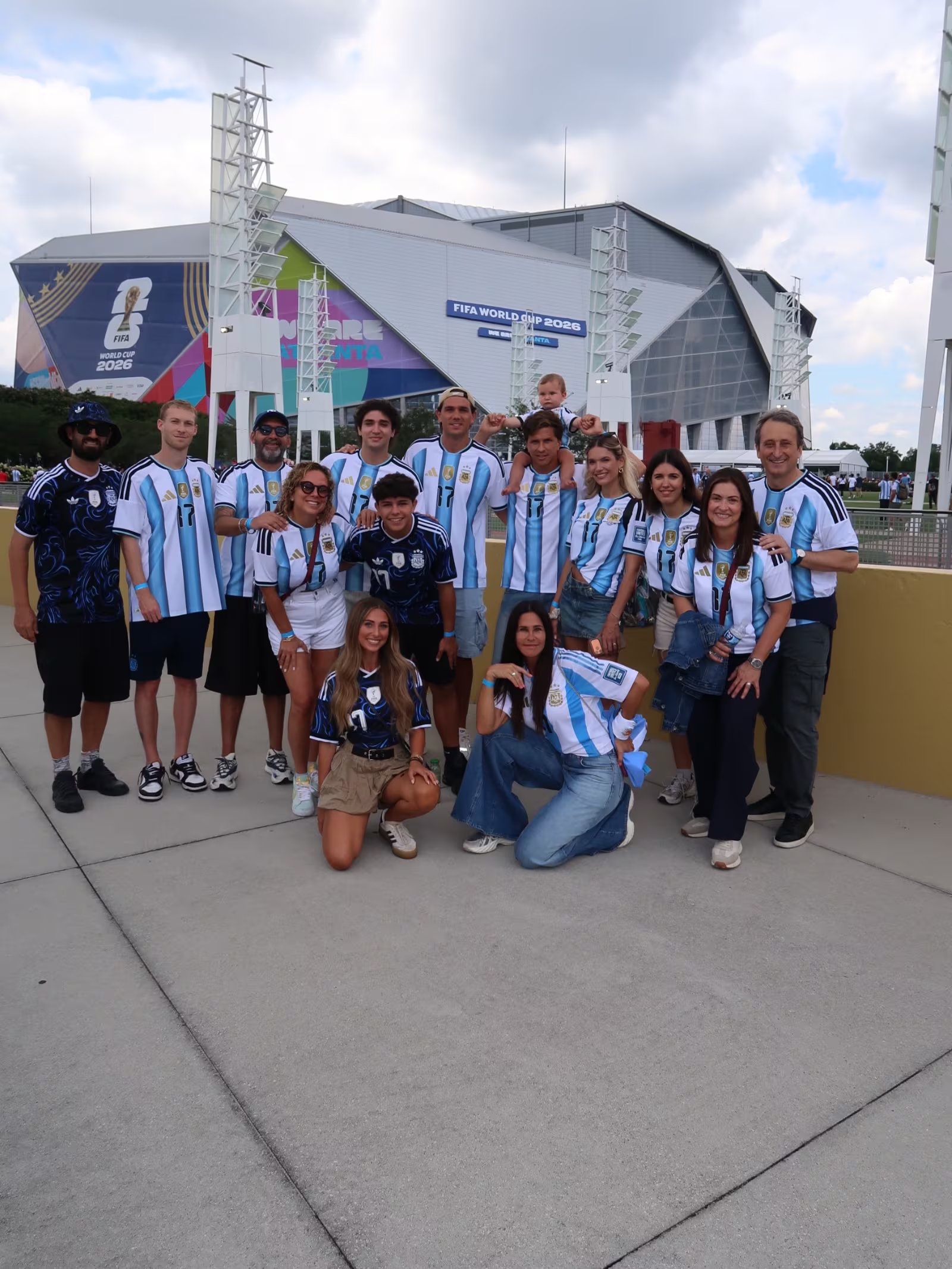 Carolina Baldini y la familia de Giuliano Simeone posan frente a un estadio del Mundial 2026 con camisetas de la selección argentina.