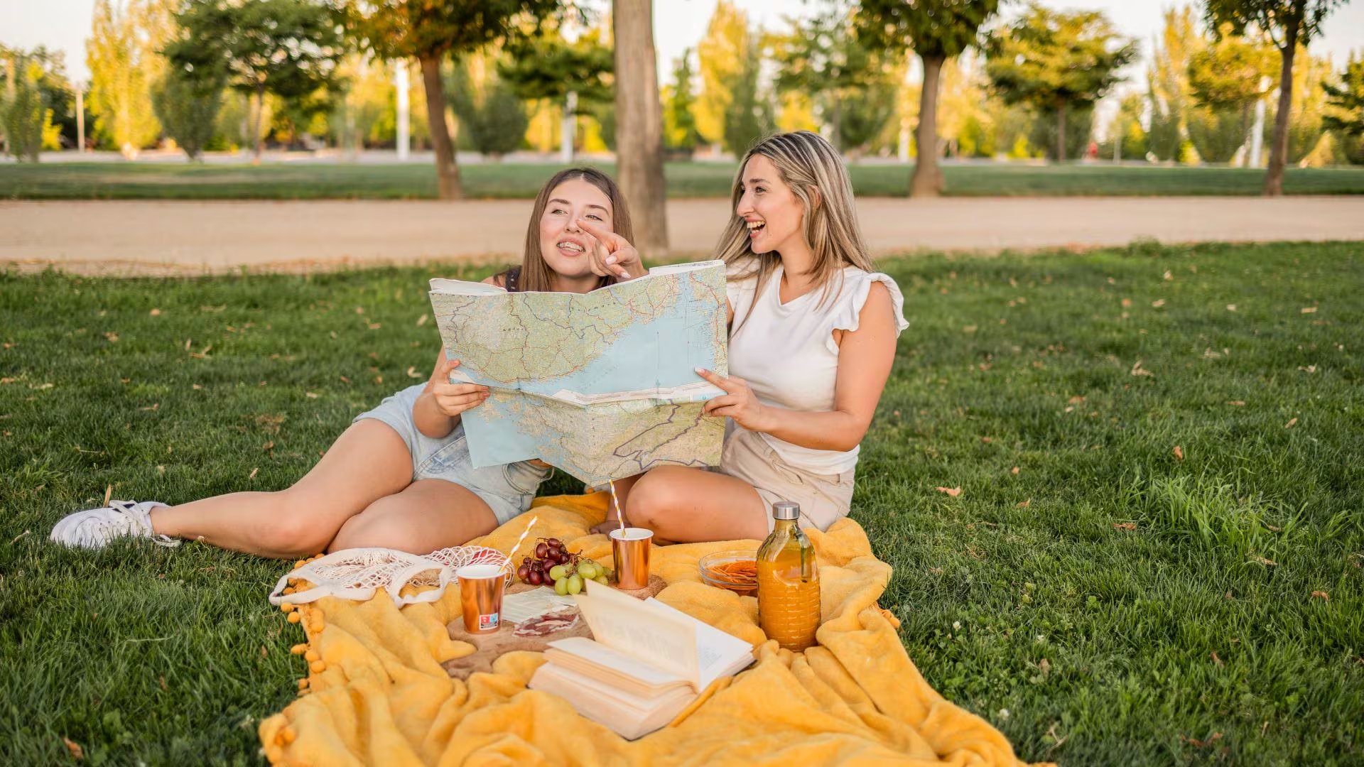 Dos amigas haciendo un picnic en un parque (Canva)