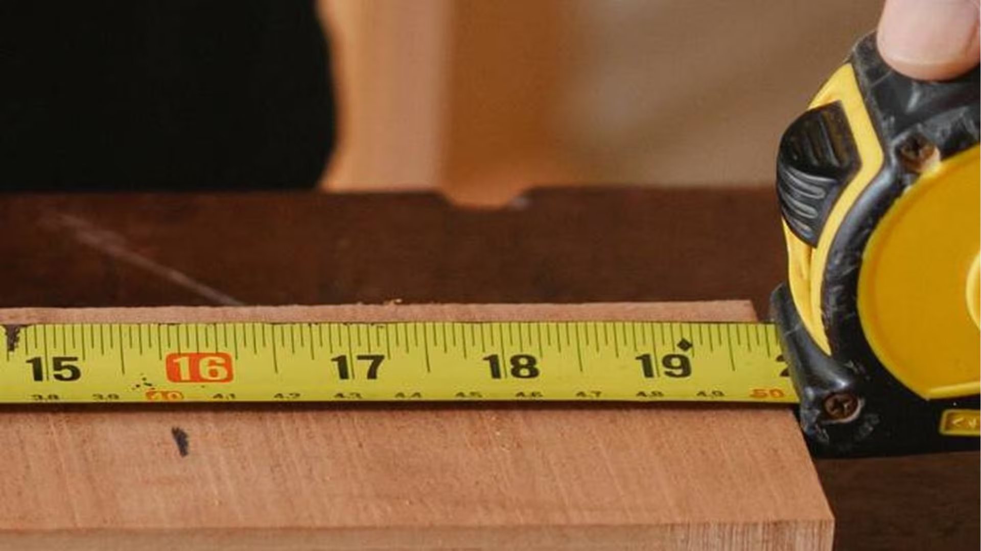 Una cinta métrica con el número dieciséis resaltado en rojo se extiende sobre una tabla de madera para señalar puntos estructurales en construcción.