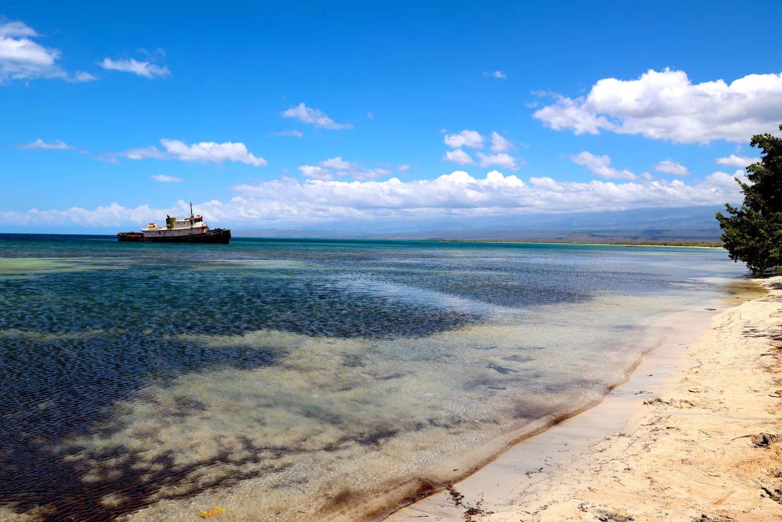 Una vieja embarcación flota en las aguas cristalinas de la costa de Enriquillo, en la provincia de Pedernales, República Dominicana, destacando la belleza natural de la región. (Cortesía)
