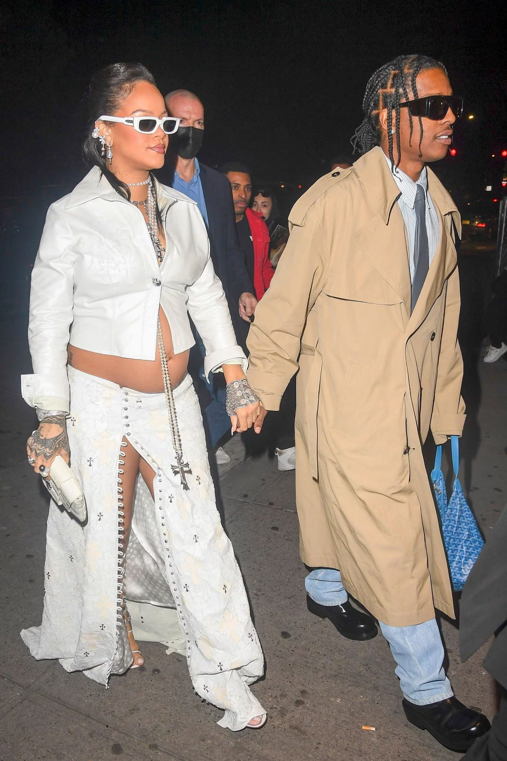 Rihanna combina blanco bordado con falda larga y clutch, A$AP Rocky suma trench beige, vaqueros claros y corbata negra (Backgrid/The Grosby Group)
