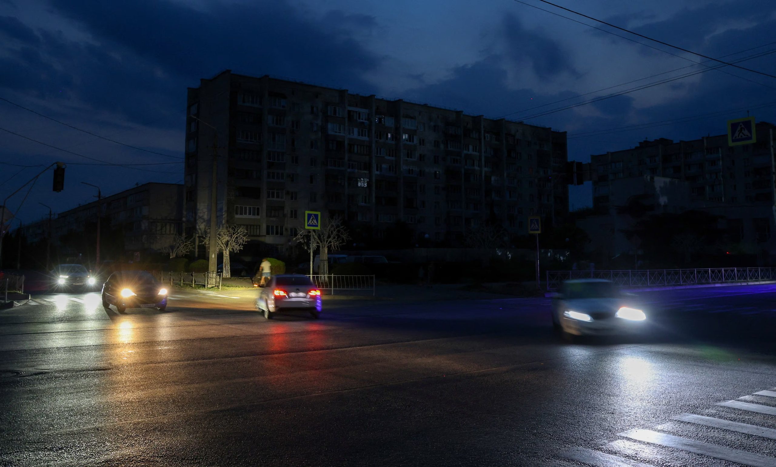 Vehículos circulan por una calle oscura cerca de edificios residenciales durante un corte de electricidad temporal (REUTERS/Alexey Pavlishak)