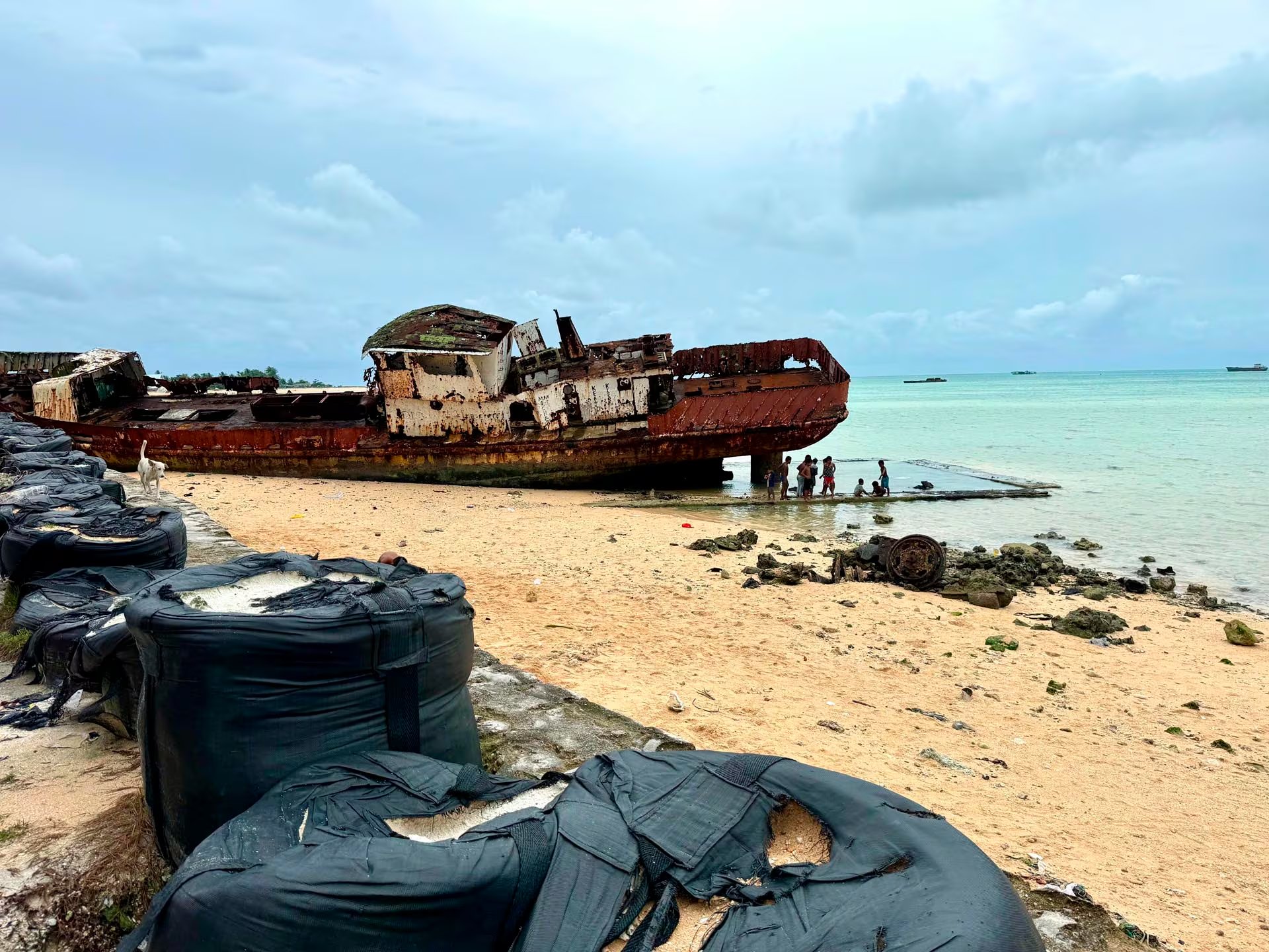 Un barco naufragado, corroído por el óxido, reposa en una playa de Tarawa. También se observan unos bolsones de arena para contener la subida del mar