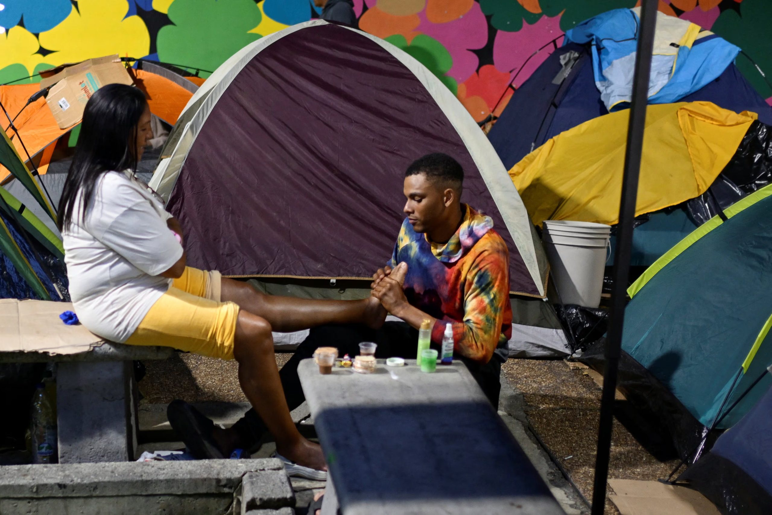 Un hombre da un masaje en el pie a una mujer mientras las personas desplazadas por los terremotos que sacudieron el país el 24 de junio viven en tiendas de campaña en un parque de Caracas, Venezuela, el 1 de julio de 2026 (REUTERS/Maxwell Briceno)